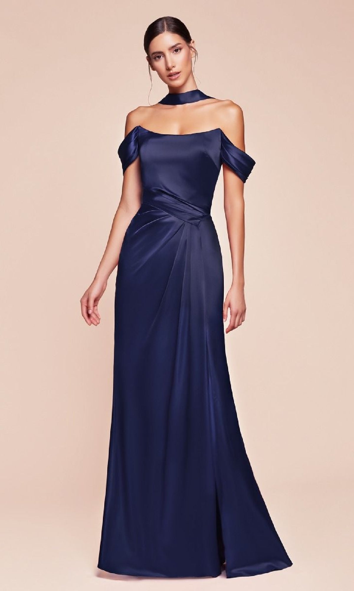 A woman wears the Ladivine 7452 Lace-Up Off-Shoulder Prom Dress— a navy blue satin, floor-length gown with a matching neckpiece— against a light beige background.