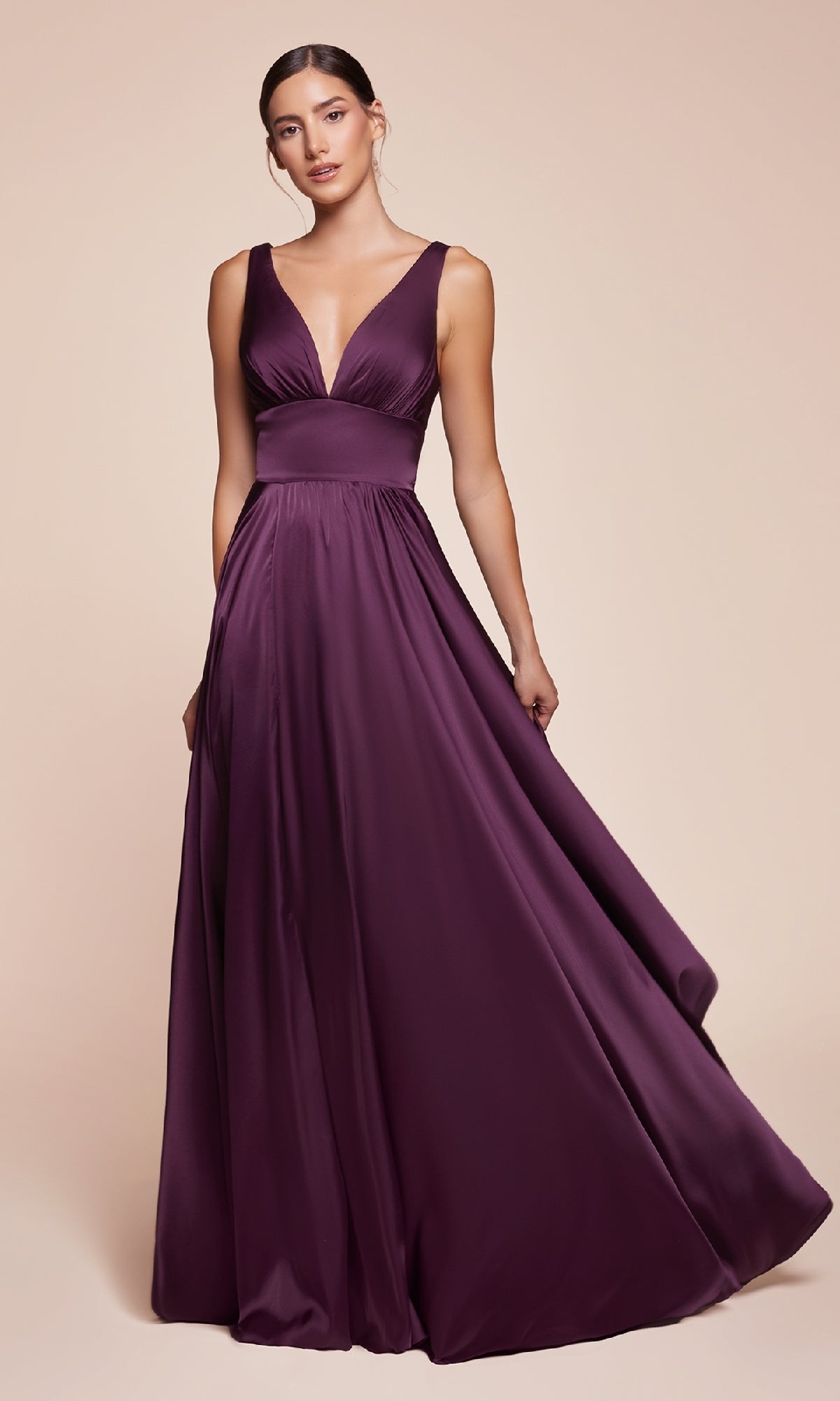 A woman stands against a beige background wearing the Ladivine 7469 Sleeveless Classic Long Prom Dress, featuring a deep v-neck and rich purple satin.