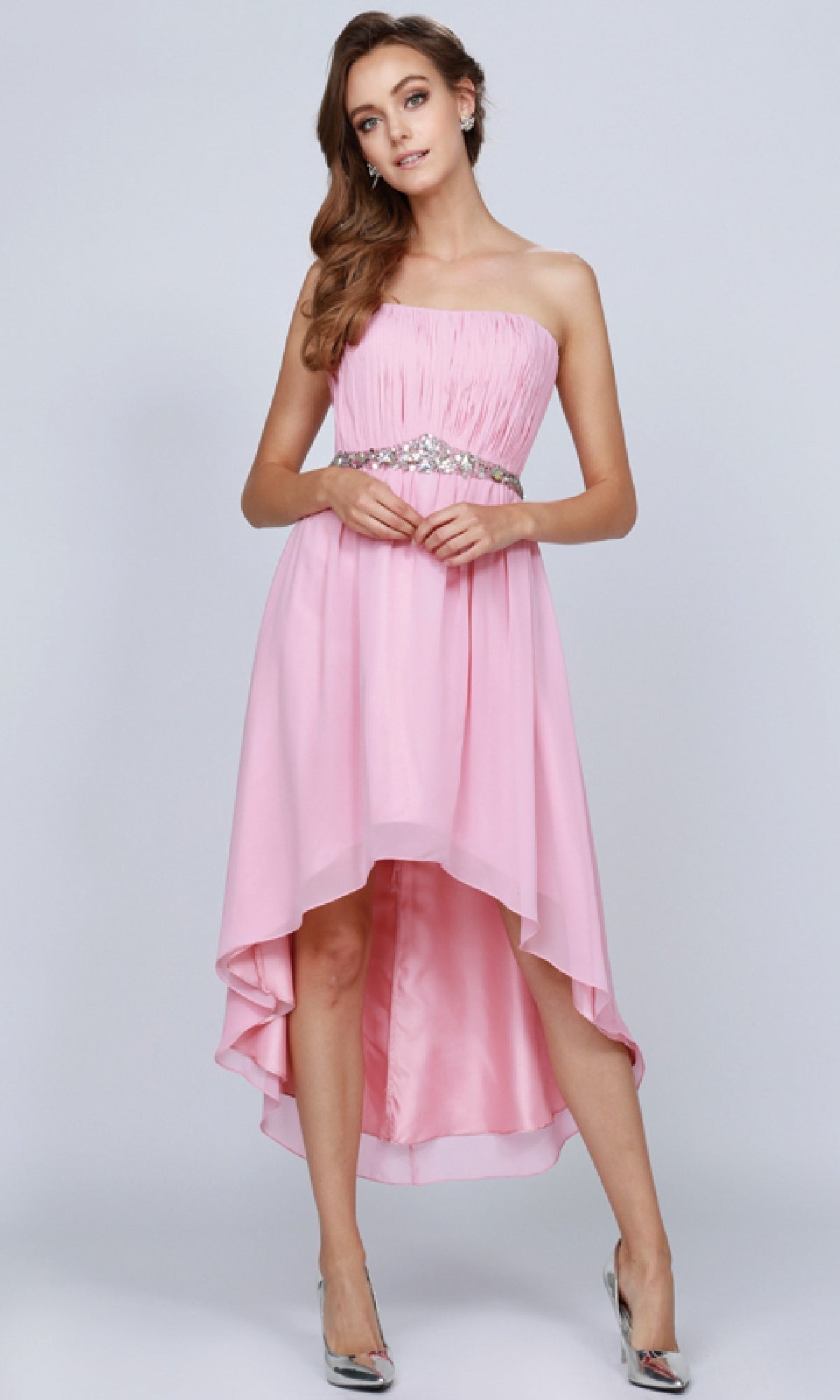 A woman models the Juliet 747 High-Low Semi-Formal Dress, featuring a strapless design and embellished waistline, paired with silver heels against a plain background.