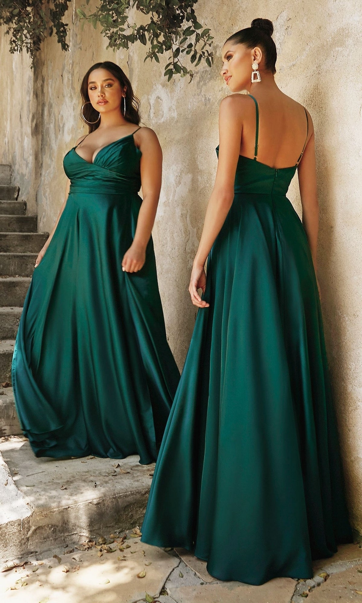 Two women showcase the Plus-Size Long A-Line Prom Dress 7485C—an emerald green, floor-length satin gown with spaghetti straps and a fitted bodice—posing near a stone wall and steps, shown from both front and back.