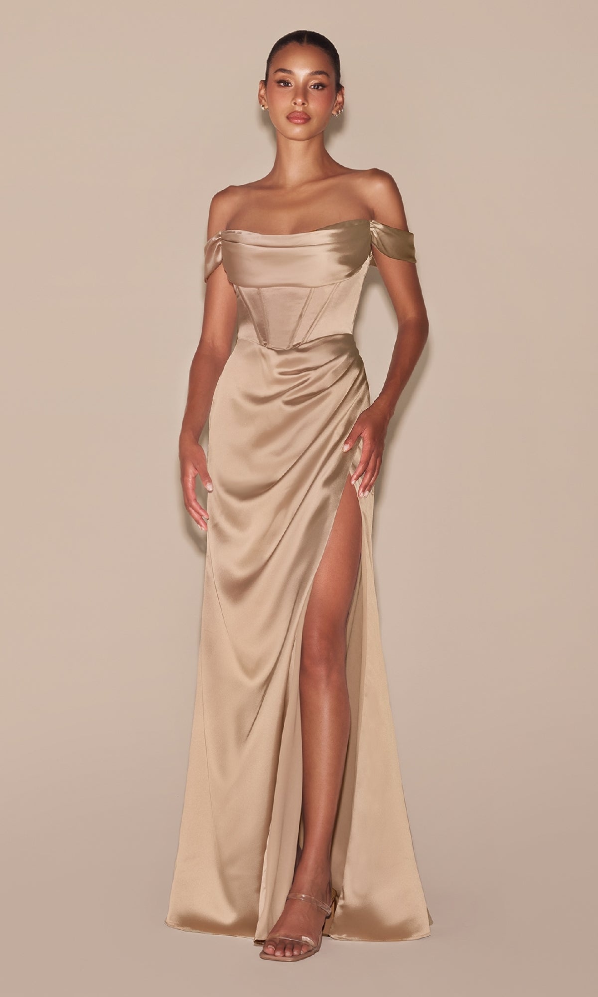 A woman models the Cowl-Neck Plus-Size Long Corset Prom Dress 7492C in champagne satin, featuring an off-the-shoulder design and thigh-high slit, paired with strappy heels against a plain beige background.