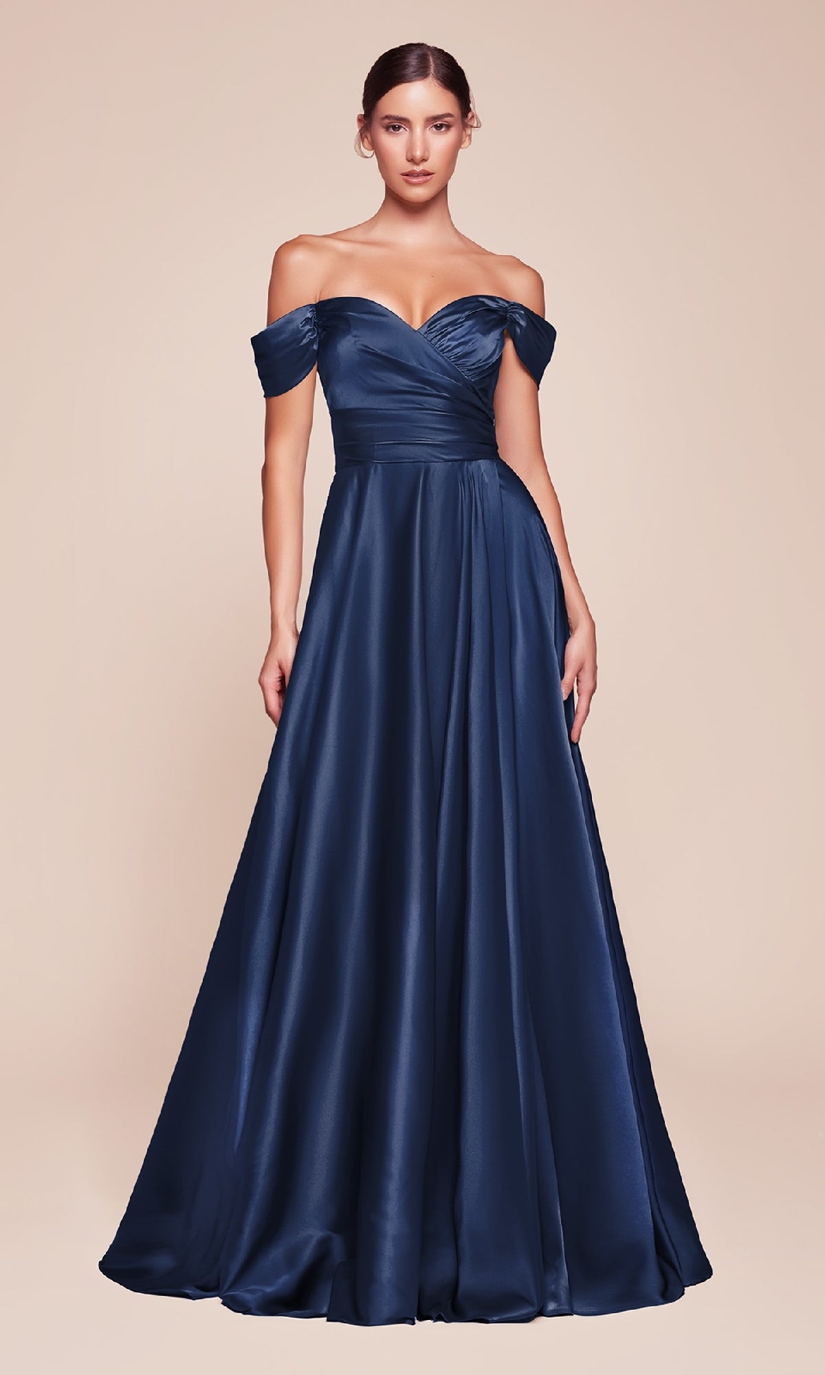 A woman models the Empire-Waist Plus-Size Long Prom Dress 7493C in navy blue satin, featuring an off-the-shoulder, floor-length design, standing against a plain beige background.