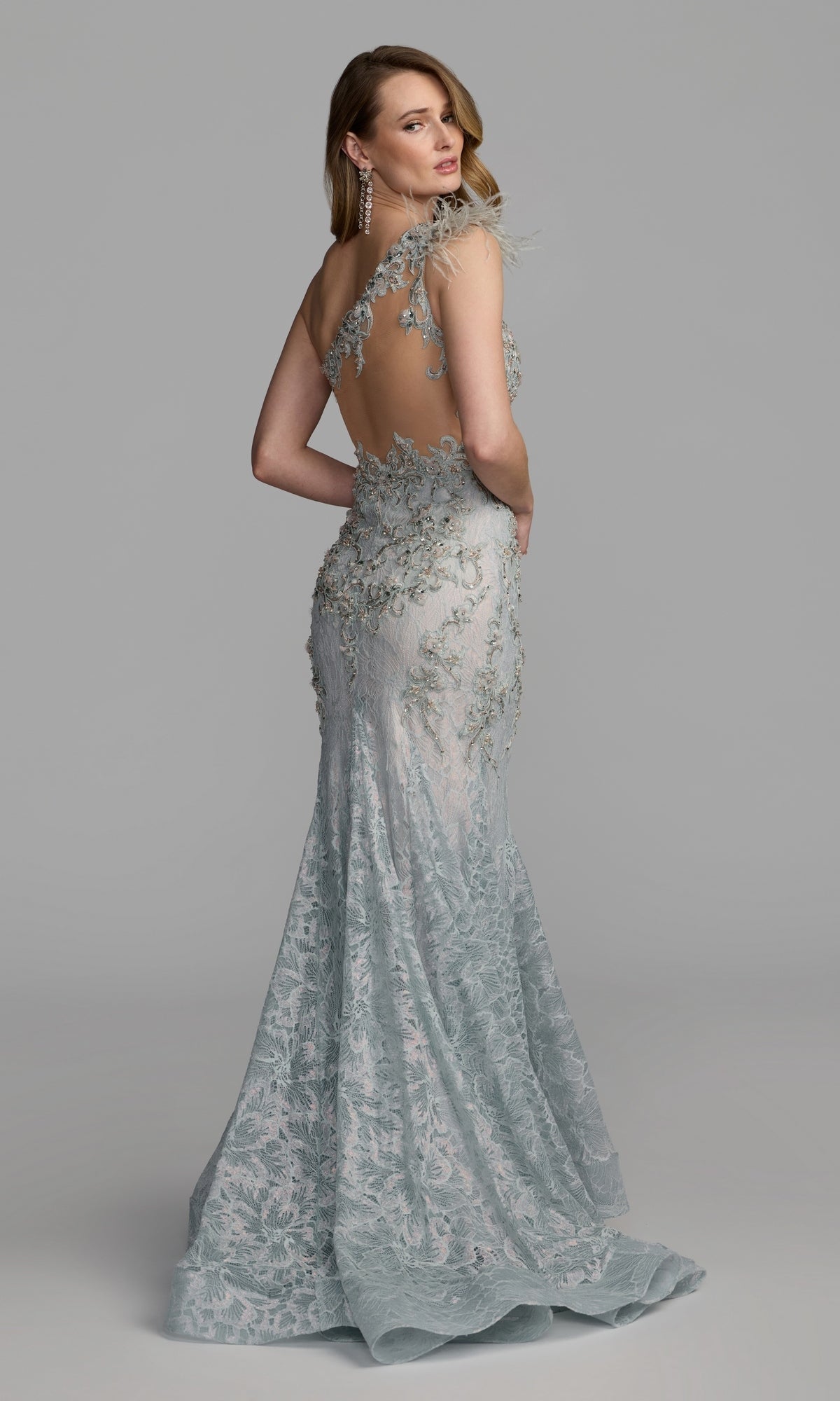 A woman stands and poses against a plain gray background wearing the Feather One-Shoulder Prom Gown: Mac Duggal 79264—a light blue, backless mermaid dress adorned with delicate lace, floral embroidery, and shimmering beaded detailing.