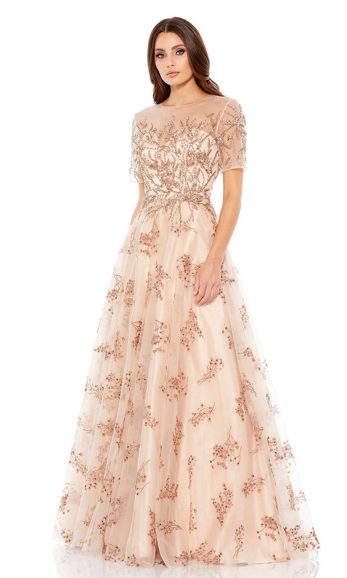 A woman wears the Long Formal Dress 79317 by Mac Duggal, a floor-length light pink A-line gown with short sleeves and intricate floral embroidery, standing against a plain white background.