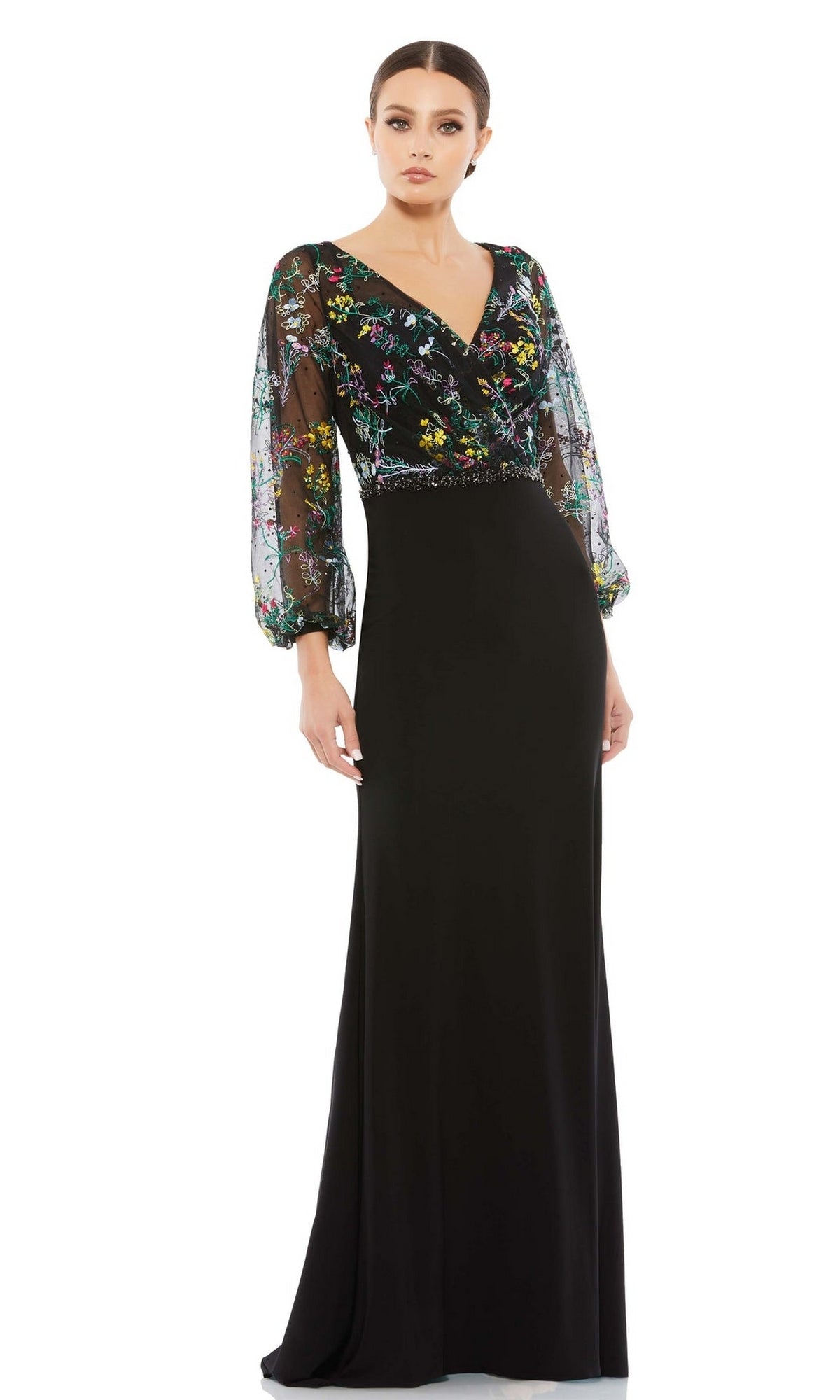 A woman wears the Mac Duggal 79379 Long Sleeve Black Formal Dress with sheer floral embroidered sleeves and a V-neckline, standing against a white background.