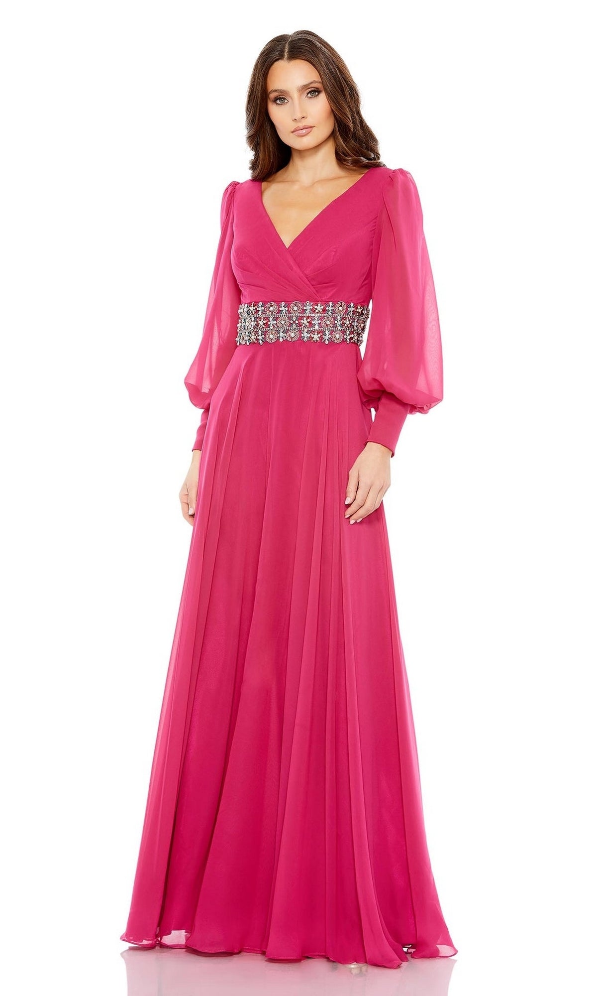 A woman models the Mac Duggal 79390: a long sleeve, bright pink formal gown with sheer puffed sleeves and a wide jeweled belt, set against a white background.