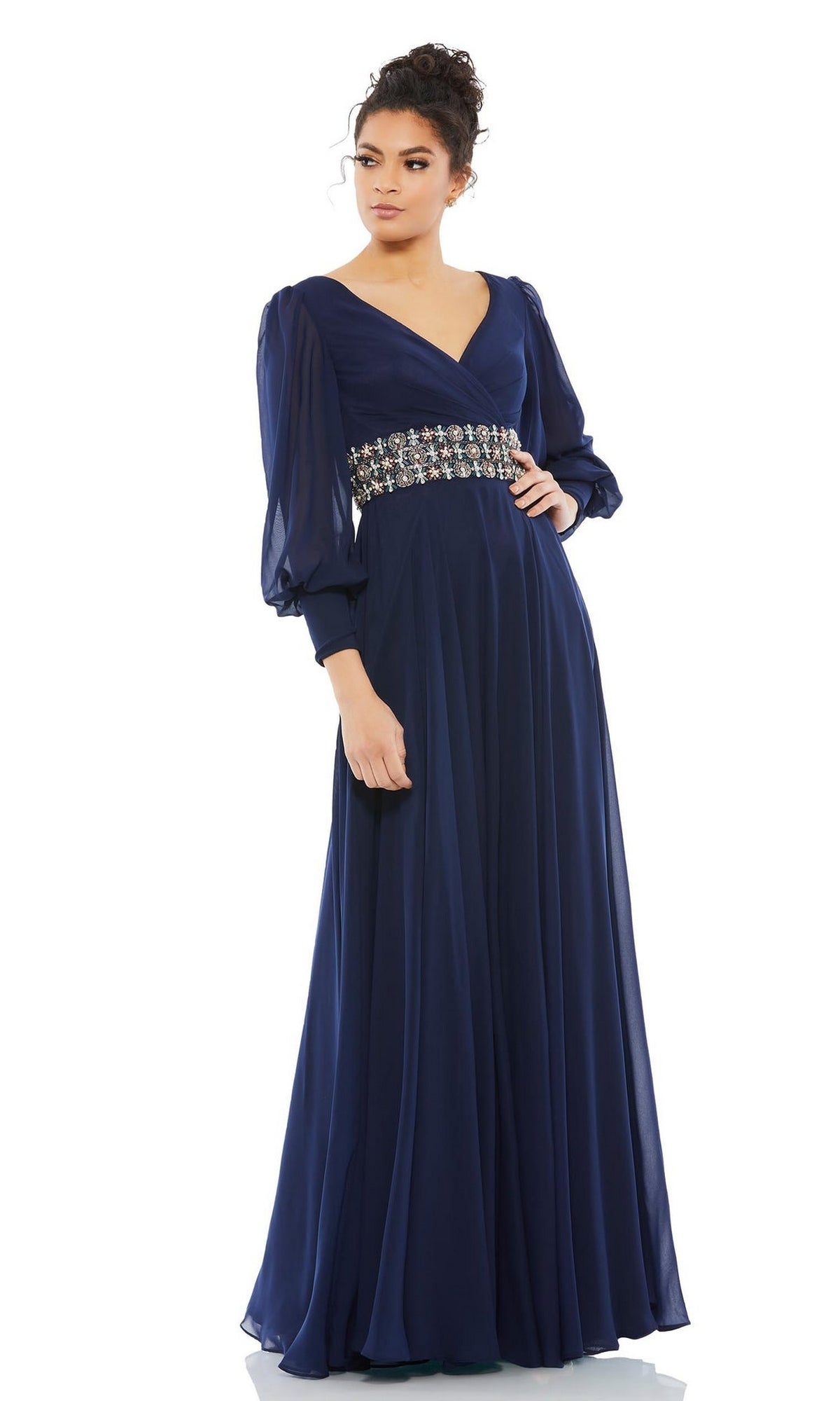 A woman models the Mac Duggal 79390 long sleeve formal evening dress in navy blue, featuring sheer sleeves and an embellished waistband, against a plain white background.