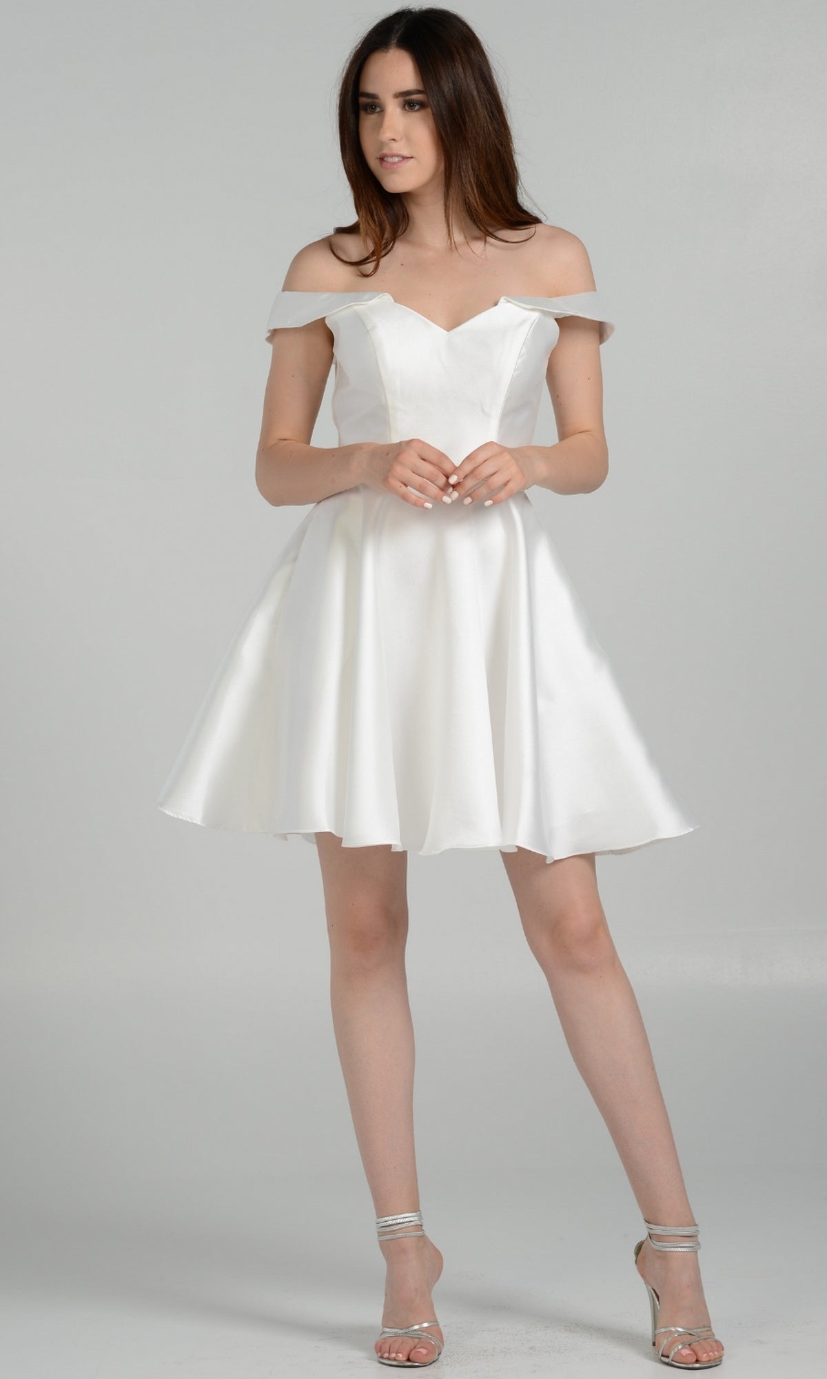A woman wears the Off-Shoulder Short Mikado Homecoming Dress 7948, featuring a flared skirt and off-the-shoulder neckline, paired with silver high heels against a plain light background.