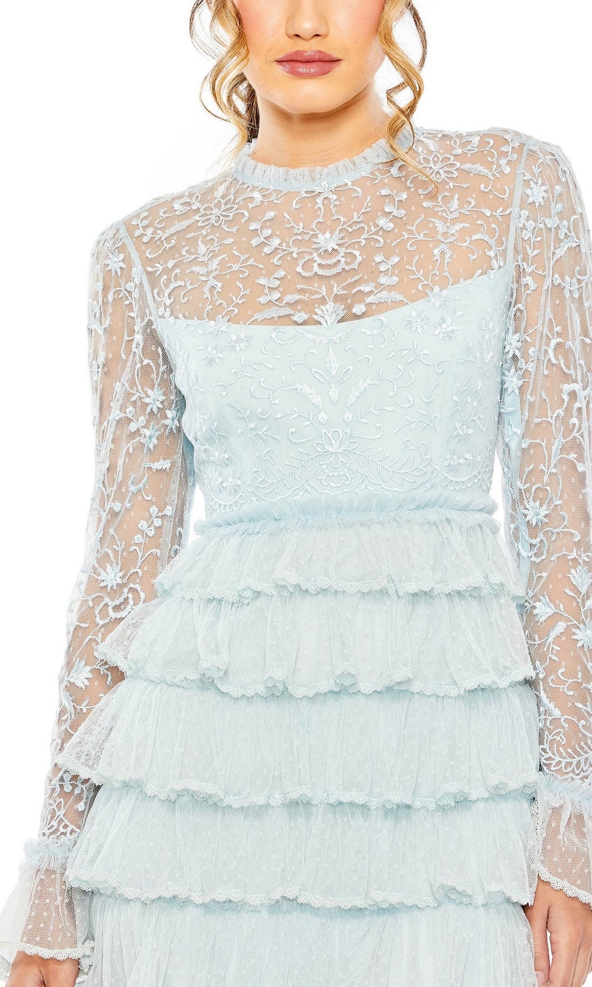 A woman showcases the Long Formal Dress 8003 by Mac Duggal—light blue lace with sheer embroidered sleeves and bodice, plus a layered ruffle skirt, shown from shoulders to thighs.
