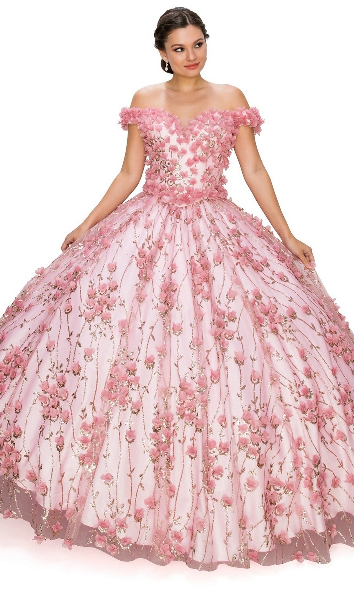 A woman gracefully poses in the Quinceanera Ball Gown 8021J—an off-the-shoulder pink dress featuring 3D floral details and a lace-up corset bodice, elegantly holding the sides of her gown.