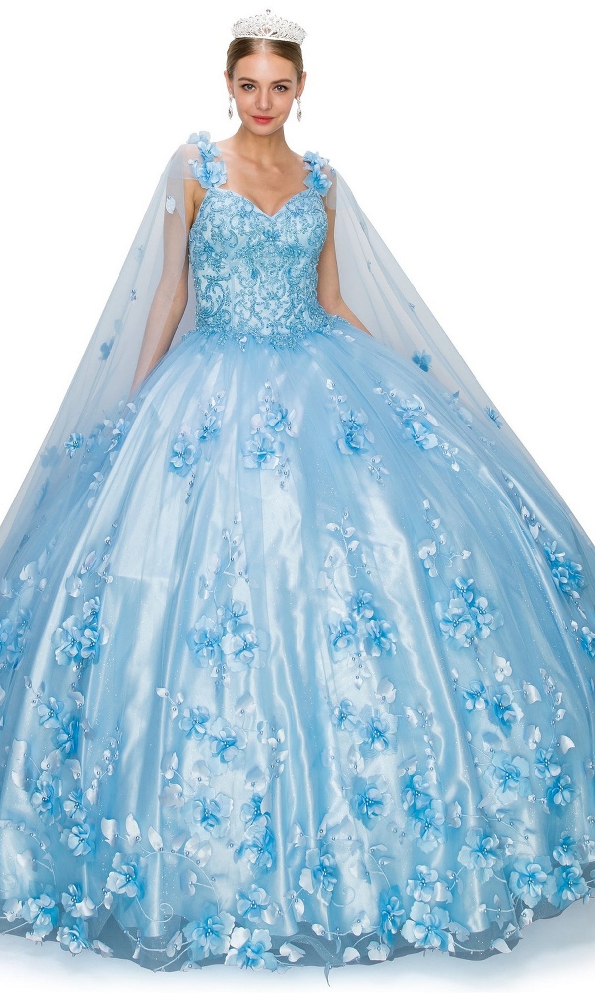 Woman wearing the Quinceanera Ball Gown 8030J in light blue with 3D floral embellishments, a cape, and tiara, standing against a white background.