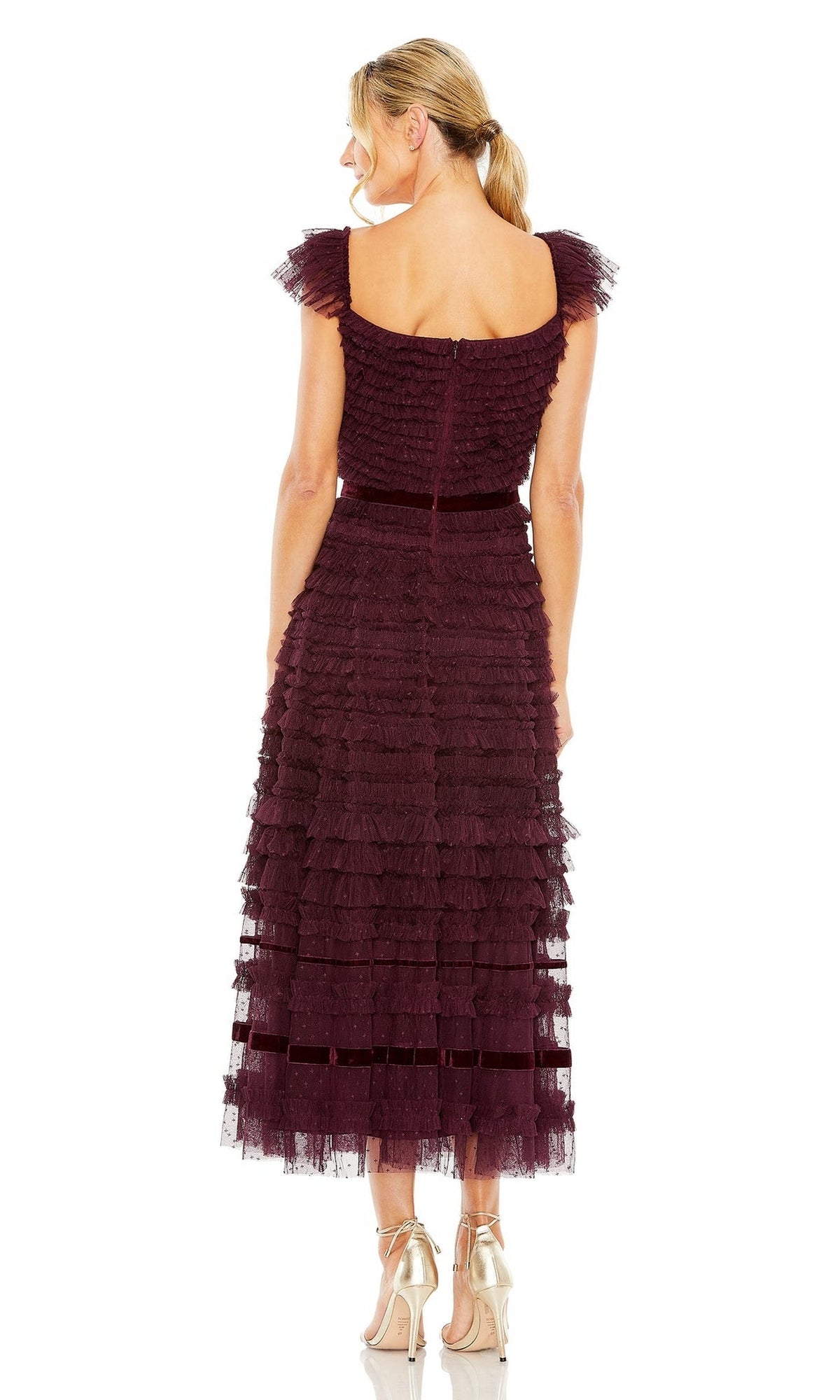 A blonde woman in a ponytail models the sleeveless Mac Duggal 8054, a burgundy tiered midi wedding guest dress, with metallic heels, standing back to camera against a white background.