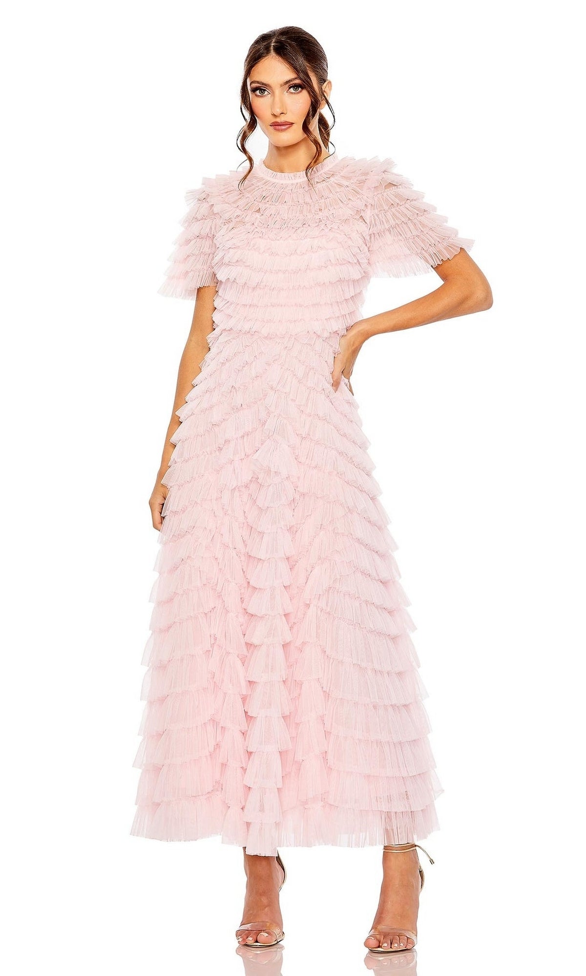 A woman wears the Midi Wedding Guest Dress 8055 by Mac Duggal, a light pink, short-sleeve midi dress with layered ruffle details, paired with strappy heels against a white background.