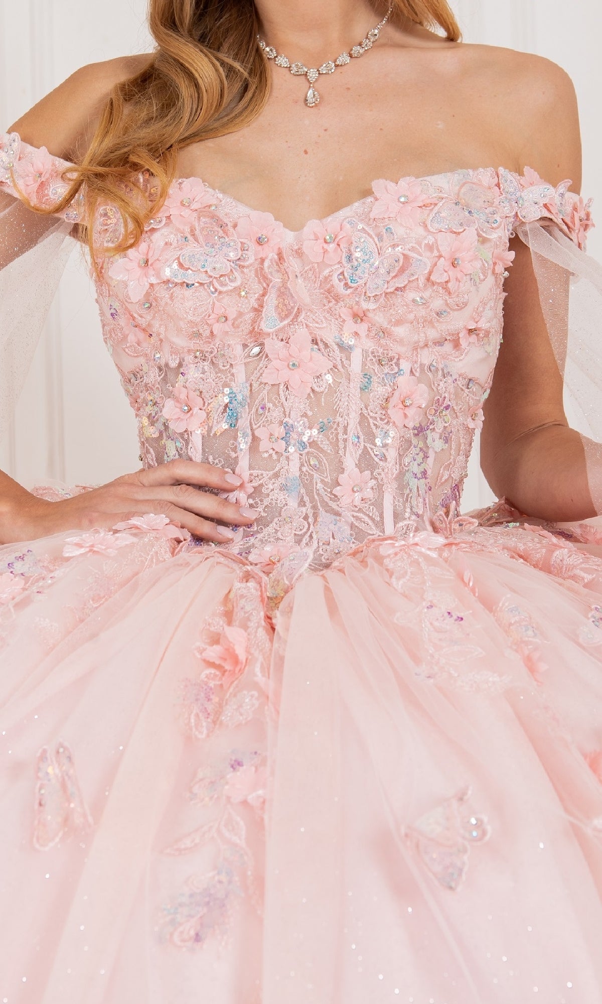 A woman wears the Cinderella Couture 8075J quinceanera dress in pink with floral embroidery, sequins, tulle details, a jeweled necklace, and a detachable sheer cape for added elegance.