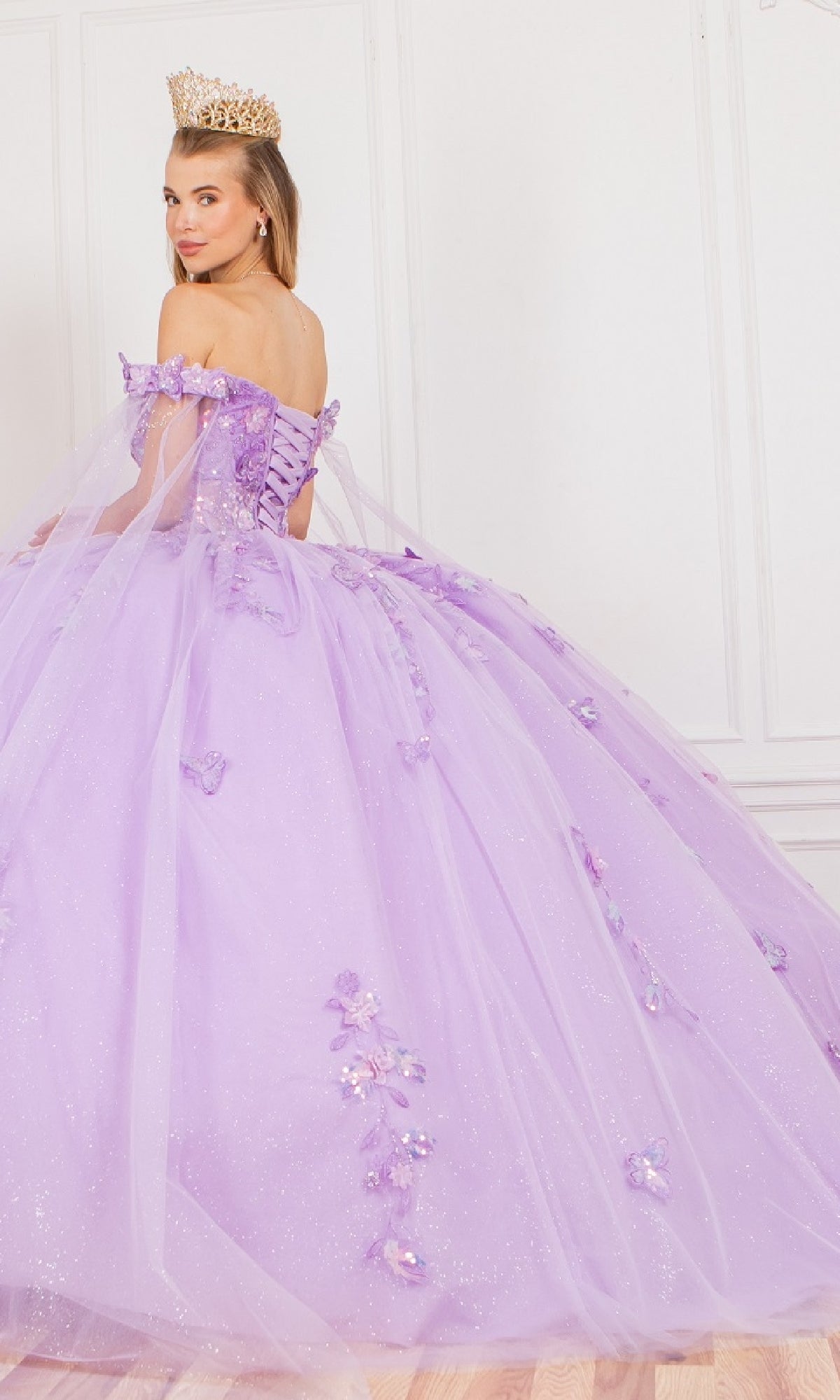 A woman wears the Cinderella Couture 8075J quinceanera dress with 3D appliques and floral details, posing indoors in a tiara while looking over her shoulder.