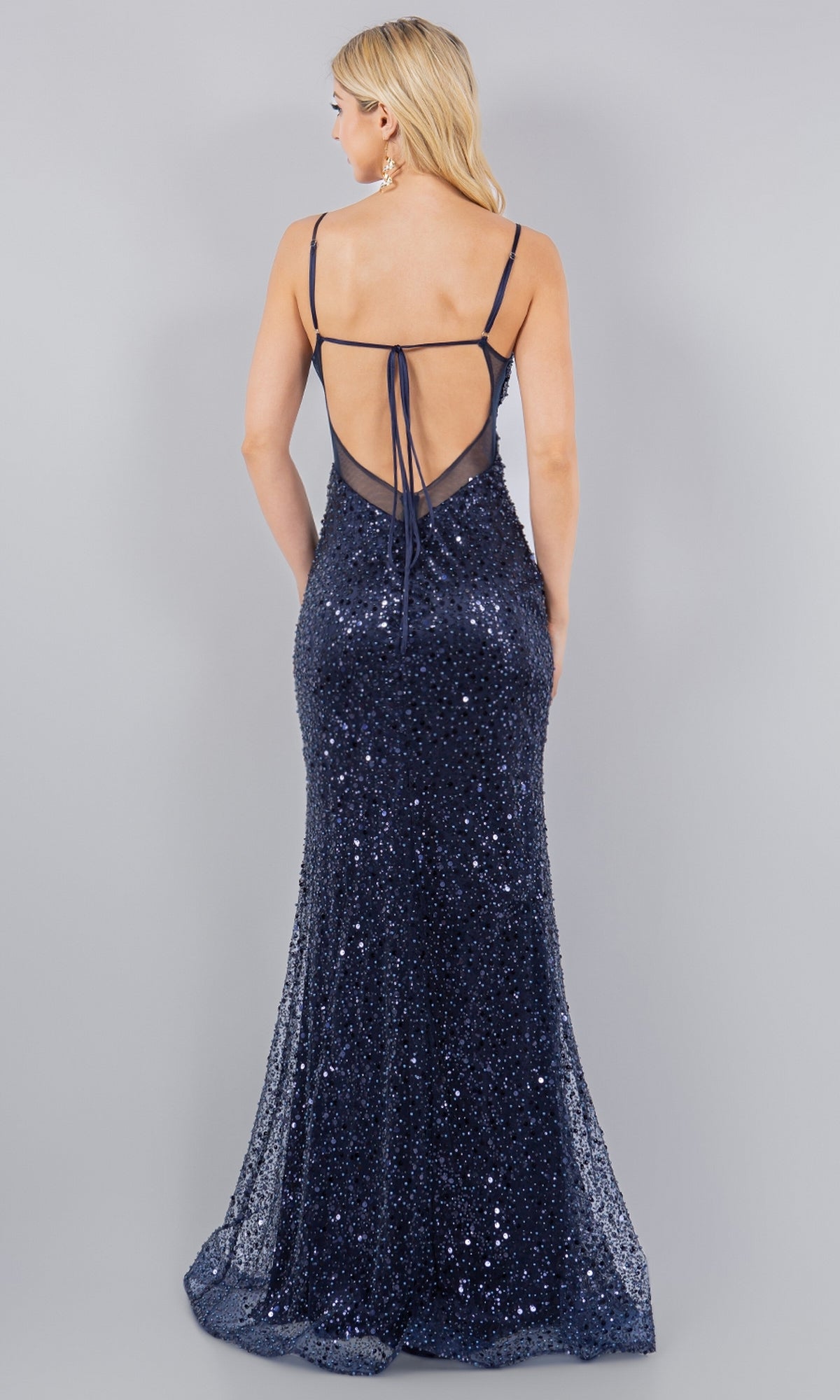 A woman models the Backless Sequin Prom Dress: Cinderella Couture 8081J—dark blue with spaghetti straps and an open back—standing against a plain light gray background.