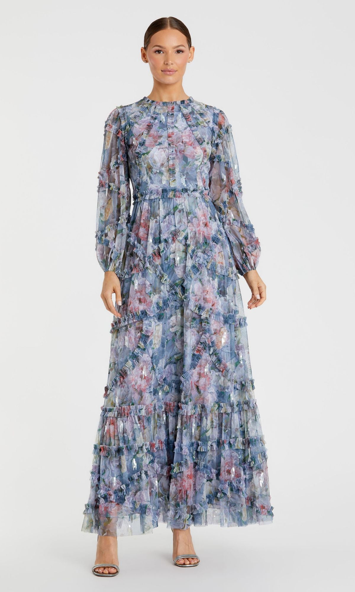 A woman wears the Mac Duggal 8098 Modest Long Print Formal Dress, featuring a blue and pink floral pattern, fitted waist, ruffled skirt, and open-toed heels.