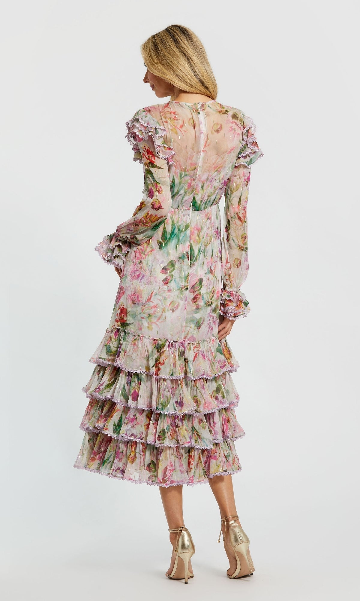 A woman faces away, wearing the Mac Duggal 8102 Midi Print Wedding Guest Dress with long sleeves and ruffled tiers, paired with gold high heels, against a plain white background.