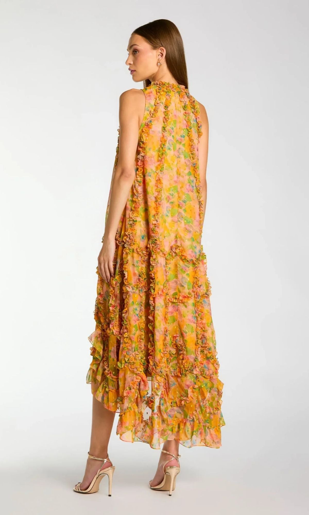 A woman faces away, wearing the Mac Duggal 8103 Midi Wedding Guest Dress— a sleeveless, floral chiffon dress with ruffled layers, paired with strappy sandals—a striking choice for wedding guests.