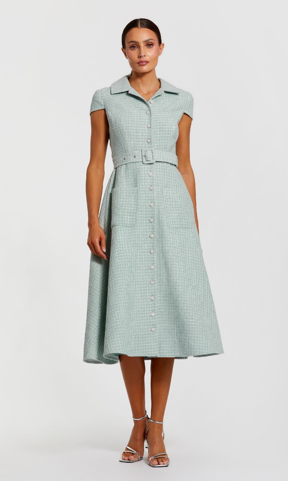 A woman stands against a white background wearing the Mac Duggal 81199 Collared Midi Green Career Dress—light green, short-sleeved, button-front with waist belt—paired with silver heels.