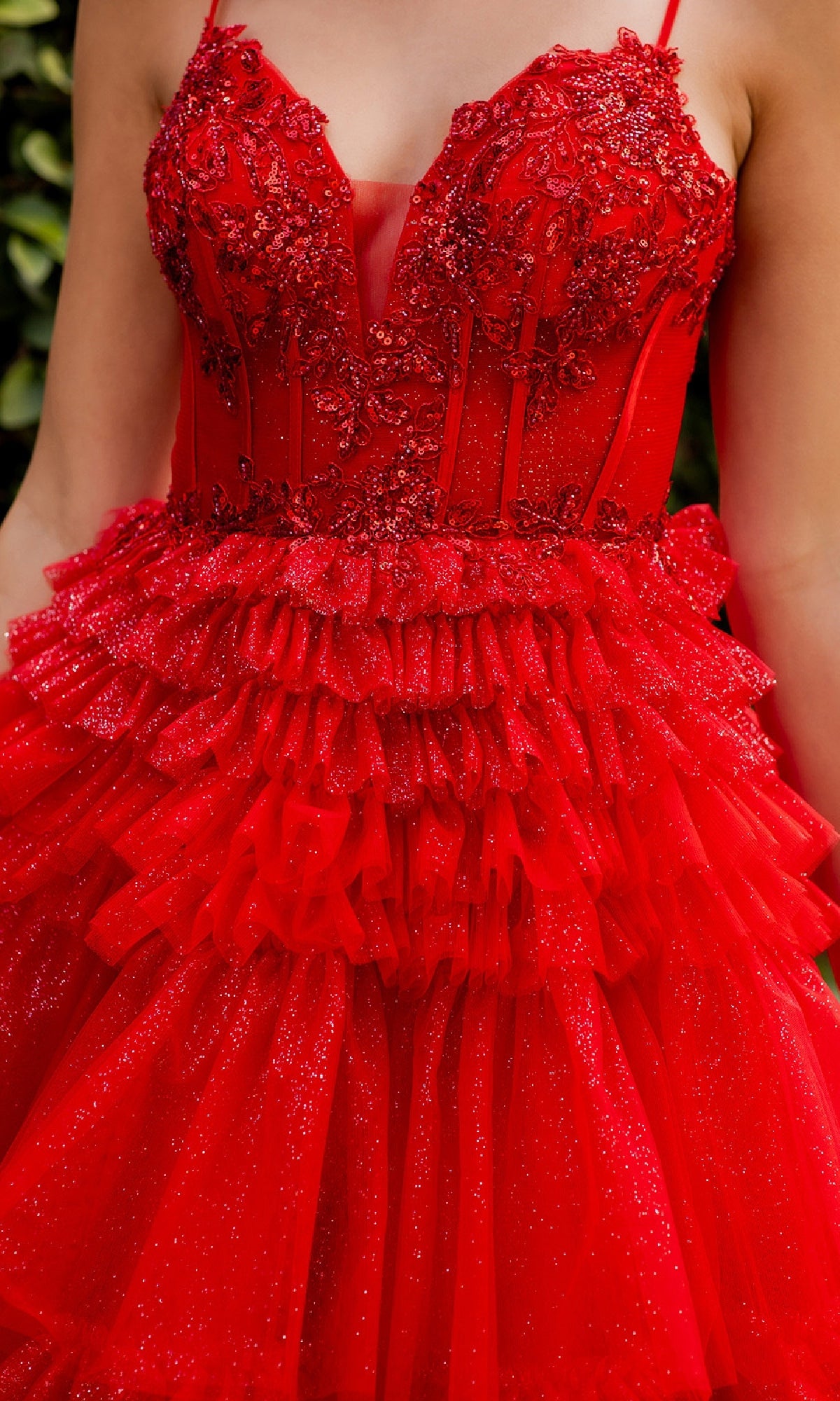 A person wearing the Glitter Prom Ball Gown: Cinderella Couture 8163J, featuring a sleeveless design, fitted beaded corset bodice, lace and bead embellishments, and layers of ruffled tulle in bright red.