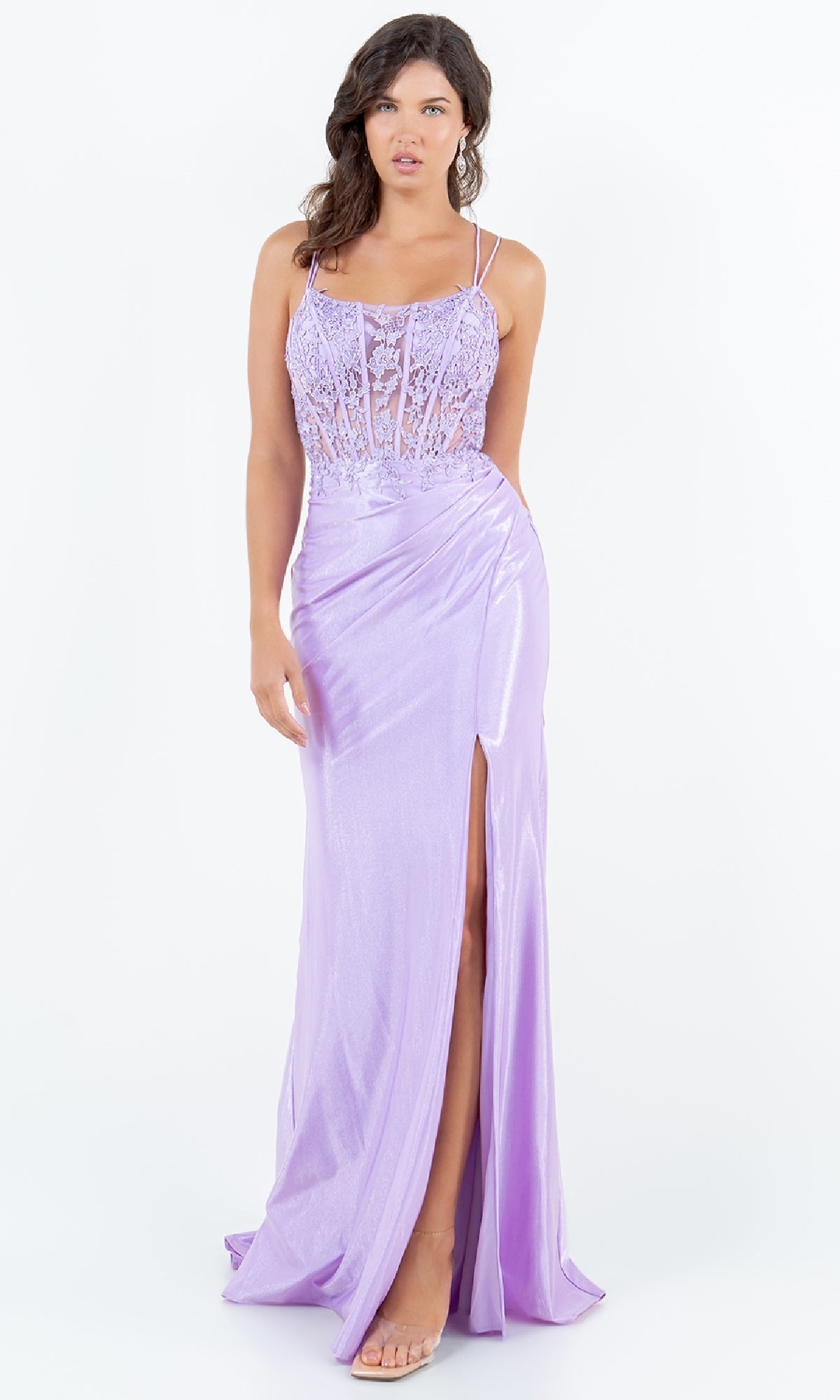 A woman models the Cinderella Couture 8185J Lace-Up Lilac Prom Gown featuring a lace bodice, spaghetti straps, and thigh-high slit, standing against a white backdrop.