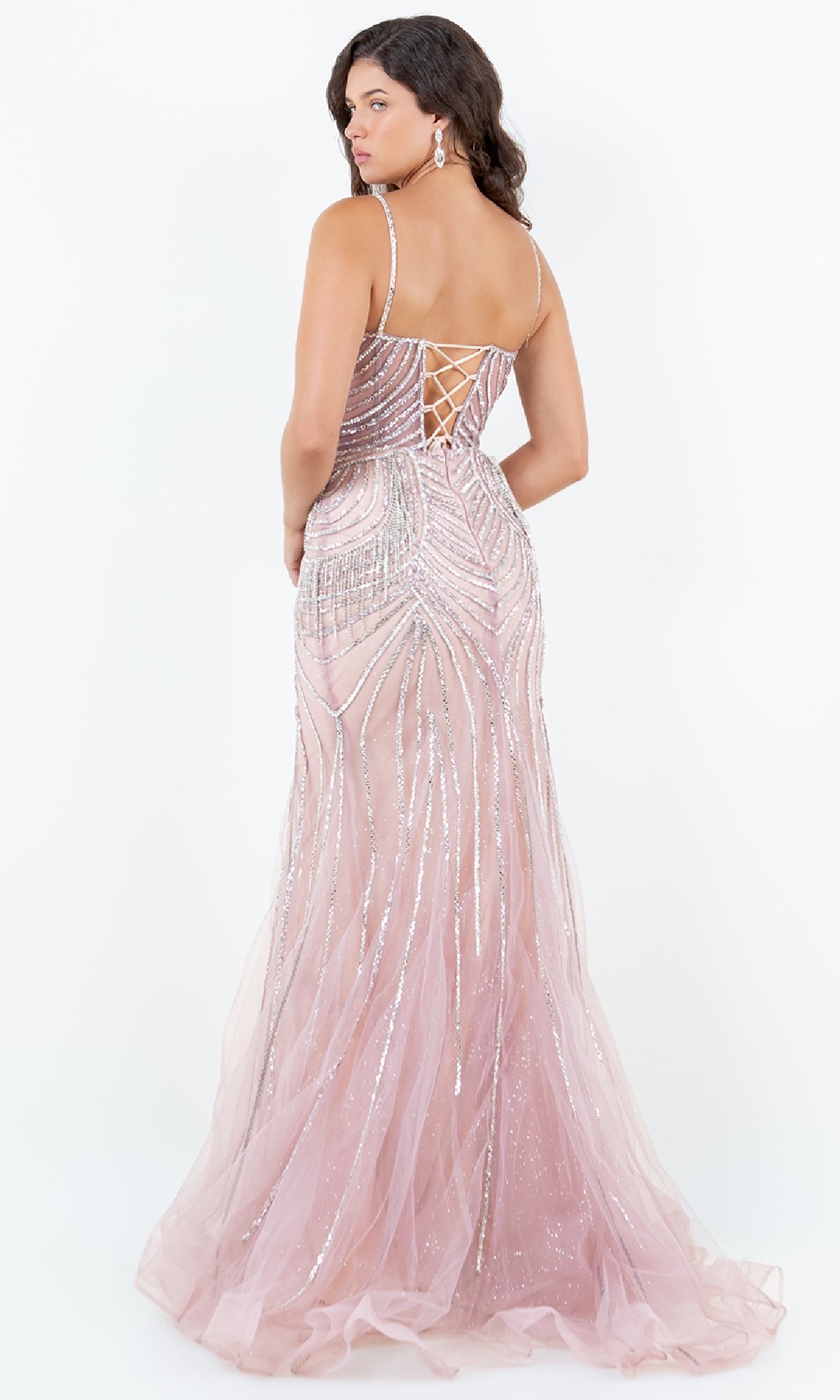 A woman wearing the Cinderella Couture 8192J Beaded Long Prom Dress, featuring light pink sparkly embellishments and a lace-up back, stands facing away from the camera.