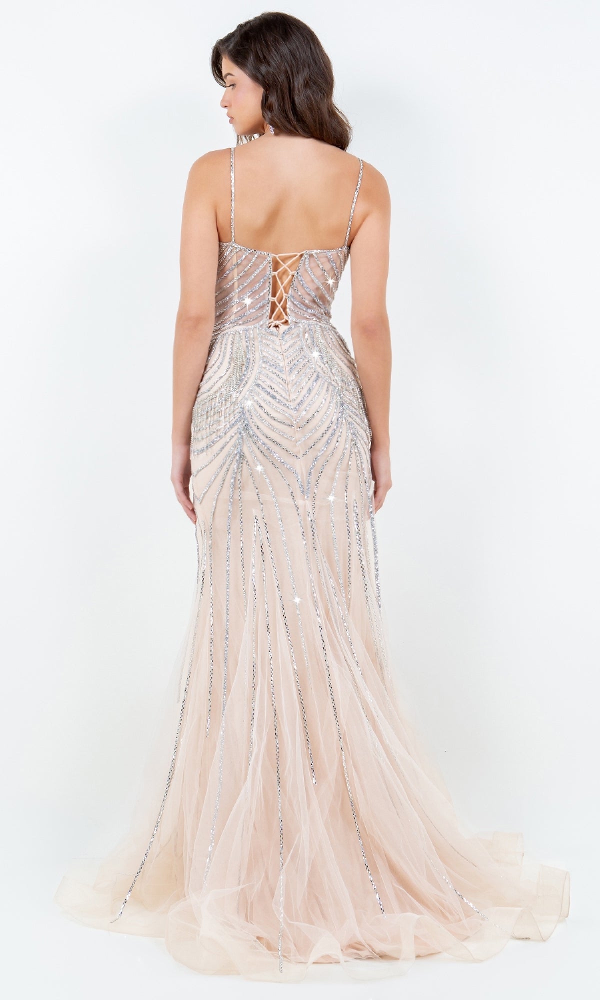 A woman wears the Beaded Long Prom Dress: Cinderella Couture 8192J, featuring a lace-up back, thin straps, and silver sequin embellishments over nude tulle—an elegant choice for any special occasion.