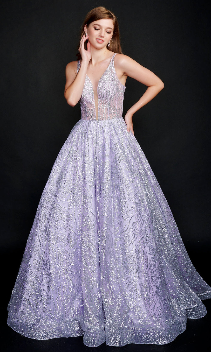 A woman stands against a plain dark background wearing the Nina Canacci 8202 Glitter-Print Ball Gown, a sleeveless, floor-length dress with a sheer bodice and sparkly textured pattern.