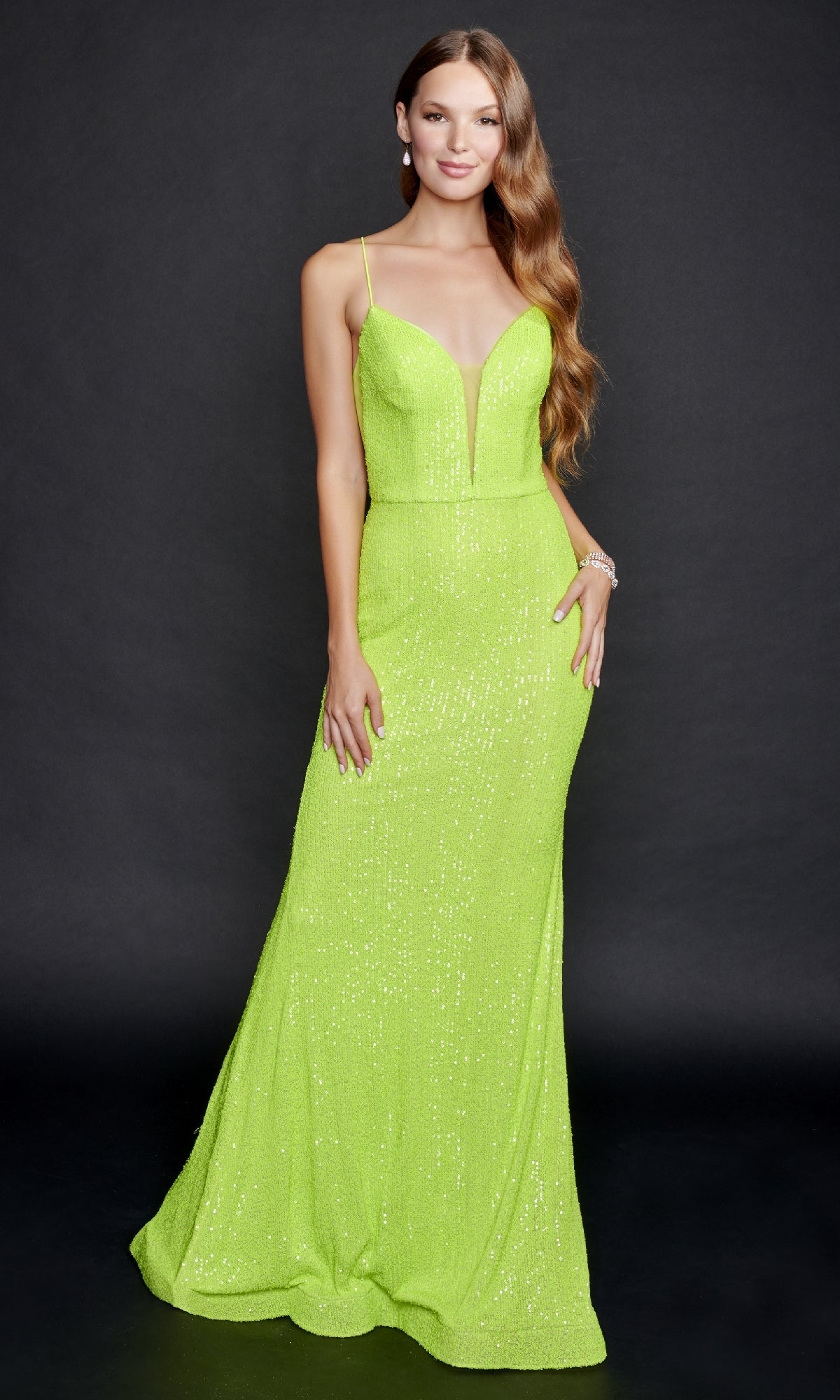 A woman stands against a black background wearing the Neon Green Sequin Prom Dress: Nina Canacci 8214, a floor-length gown with thin straps, an open back, and a deep V neckline.