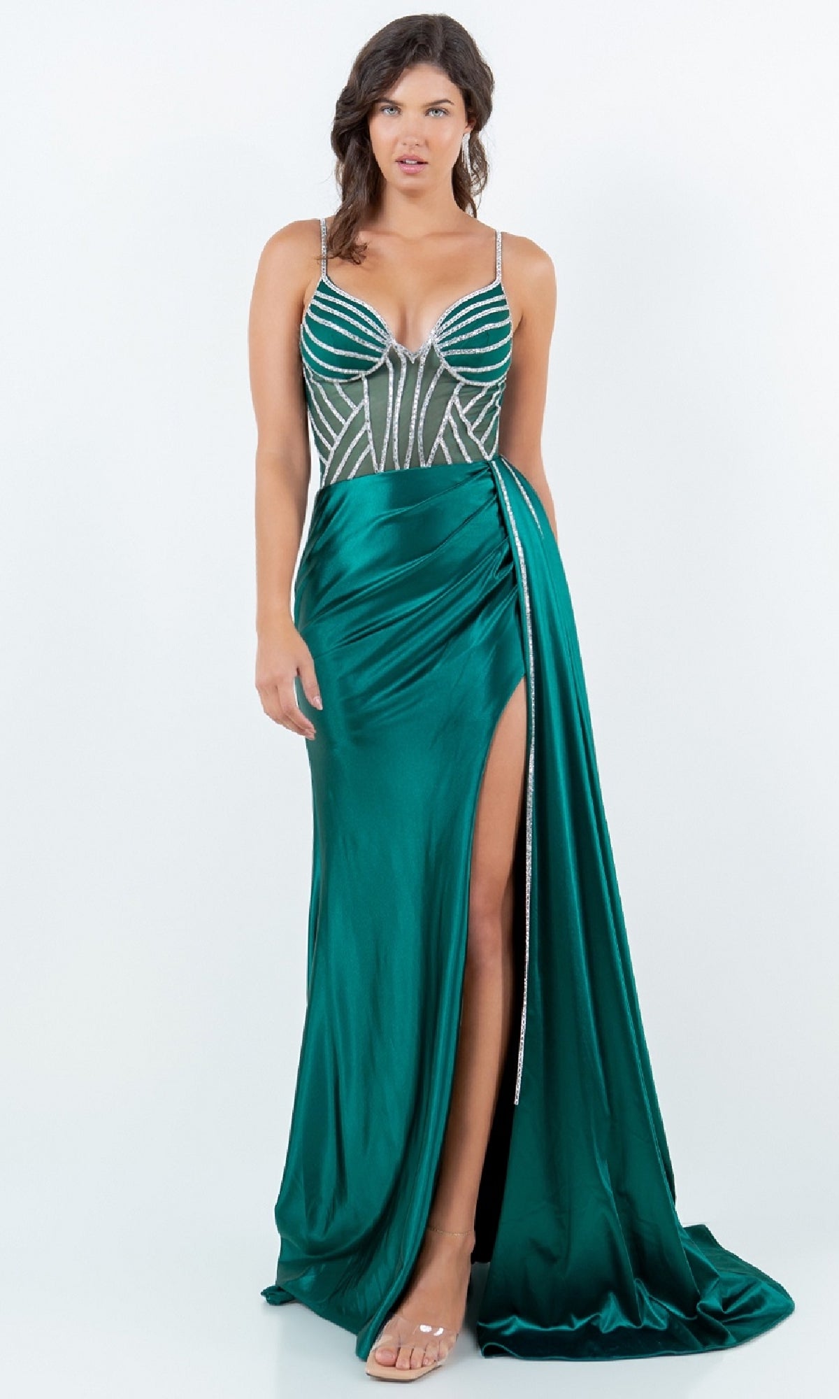 Woman wearing the Cinderella Couture 8219J Side-Sash Long Prom Gown with a thigh-high slit, beaded emerald green fabric, sheer bodice, and spaghetti straps, standing against a plain white background.