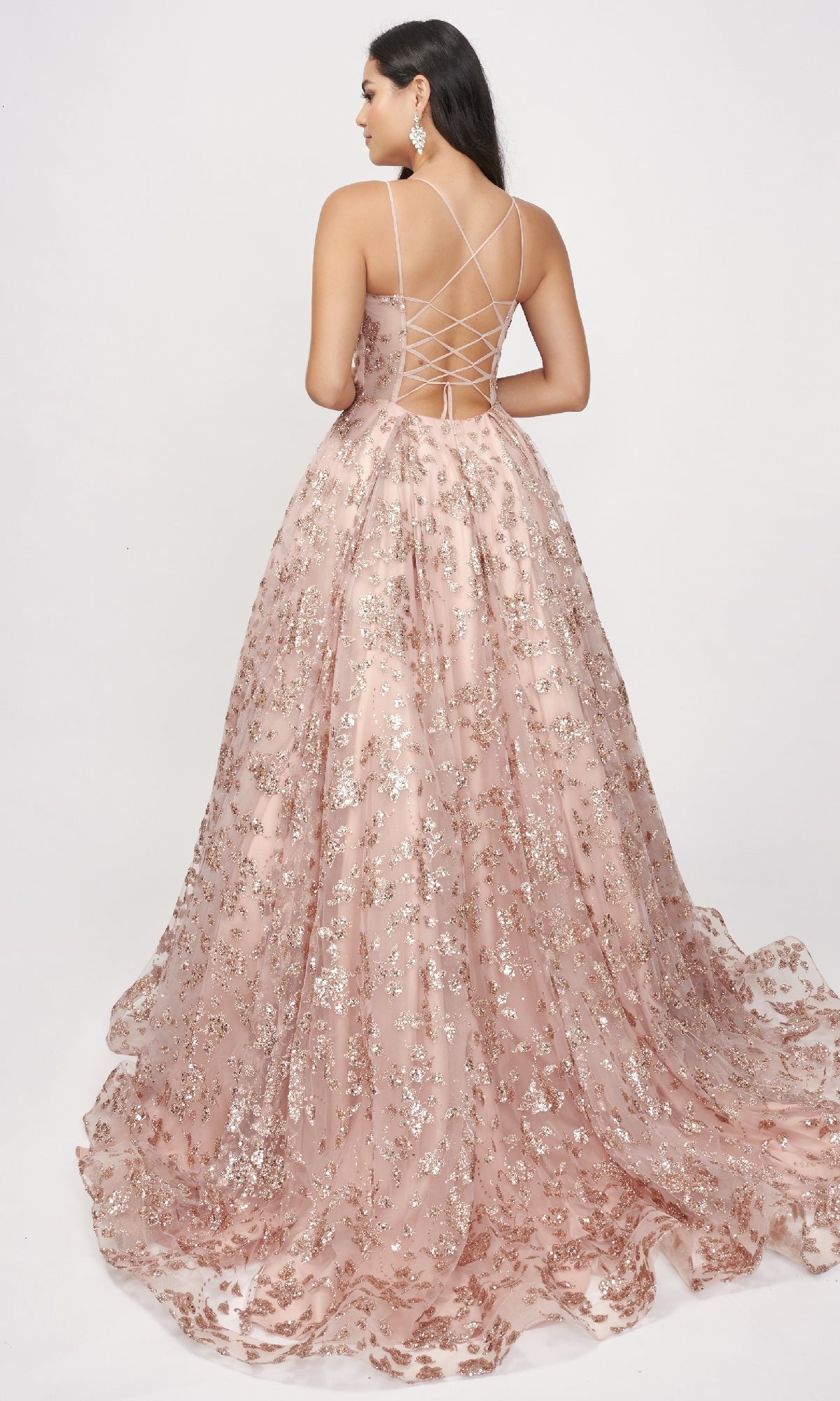 A woman models the Nina Canacci 8246 Rose Gold Prom Ball Gown, featuring silver sequins and a lace-up back, in a floor-length design against a plain white background.