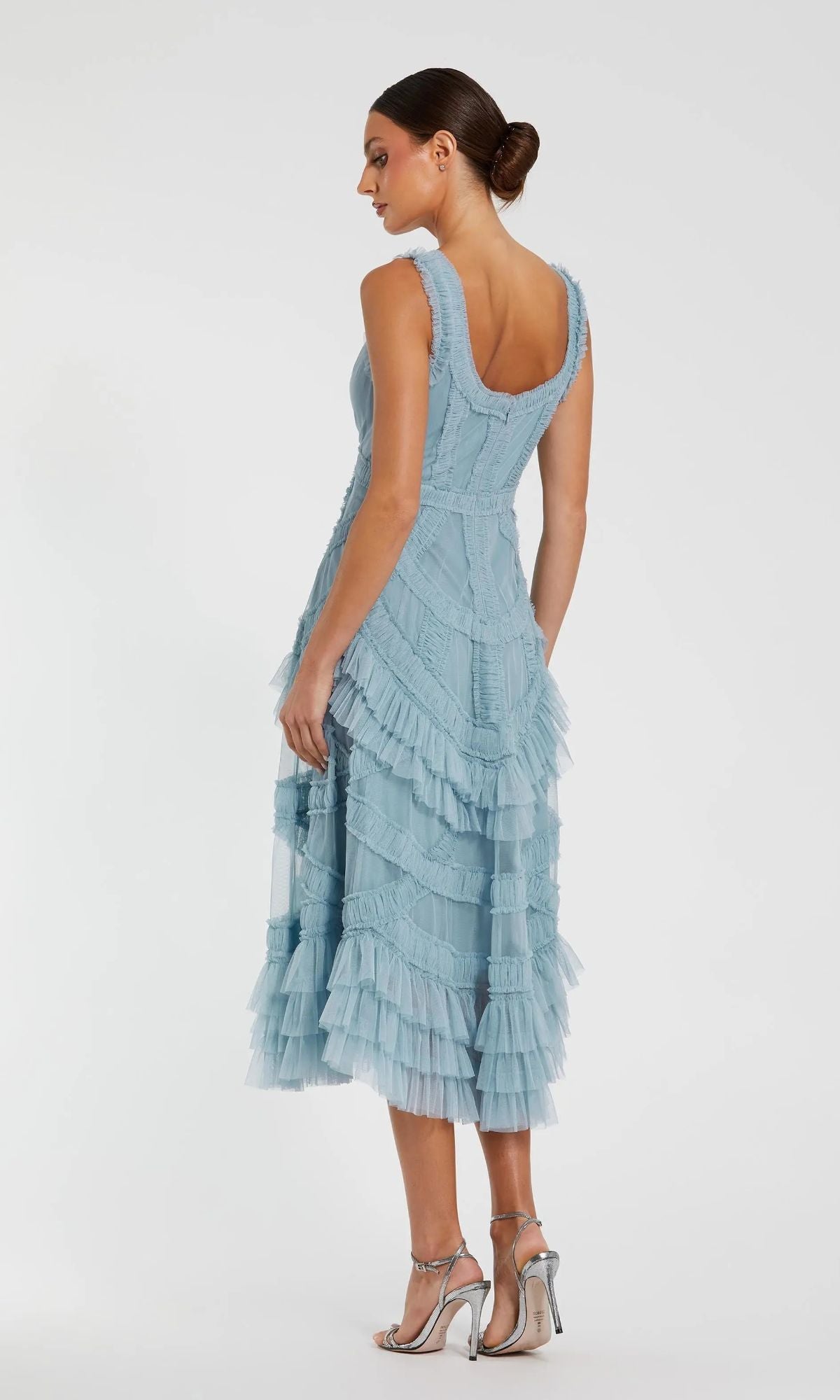 A woman in the Mac Duggal 8250 Midi Wedding Guest Dress—light blue, sleeveless, with micro ruffle details—pairs it with silver heels and a low bun for an elegant wedding guest look.