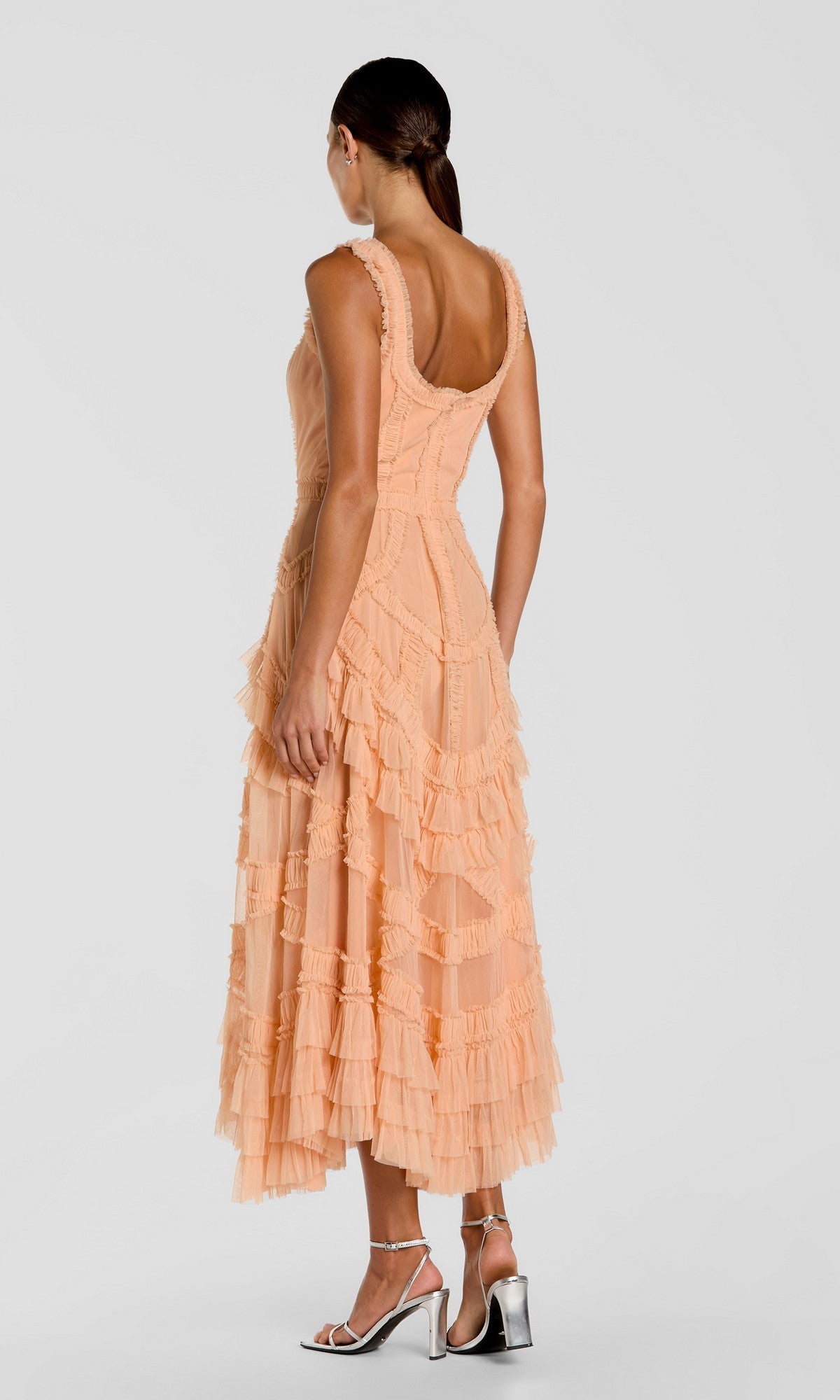 A woman faces away, wearing the Mac Duggal 8250 midi wedding guest dress with micro ruffle detailing and silver high-heeled sandals, set against a plain light gray background.