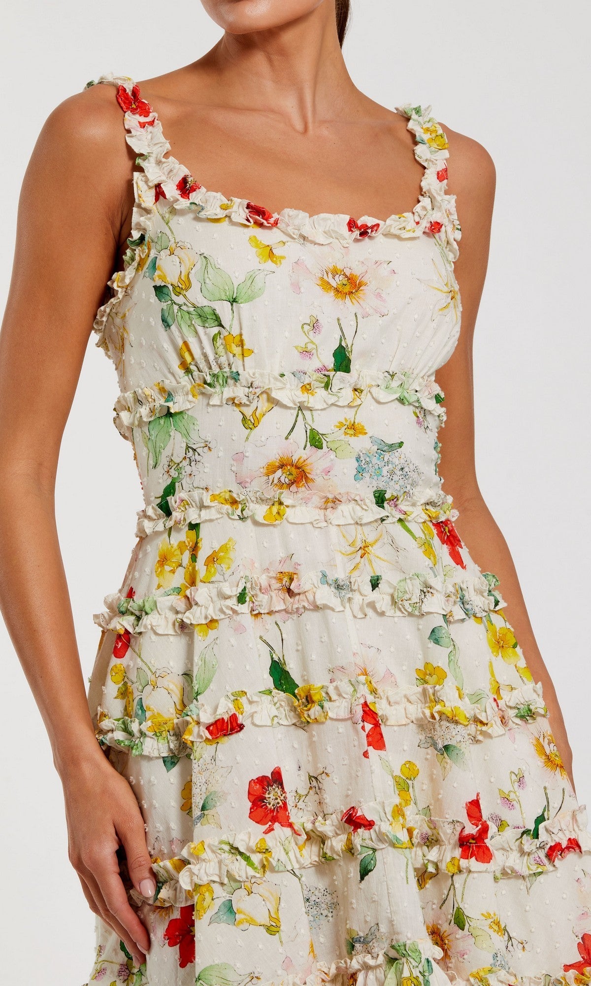 A woman models the Mac Duggal 8257 short party dress—a sleeveless cream cotton A-line design with floral print and ruffle details—against a plain background.