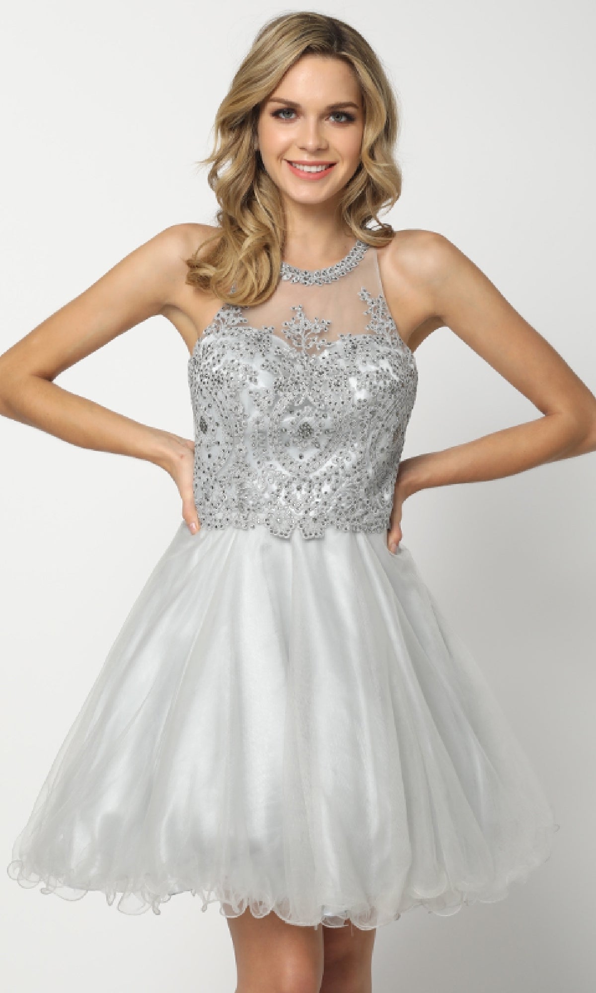 A woman models the Juliet 826 short Hoco dress, a sleeveless silver A-line babydoll with beaded bodice, sheer neckline, and tulle skirt, standing against a plain white background.