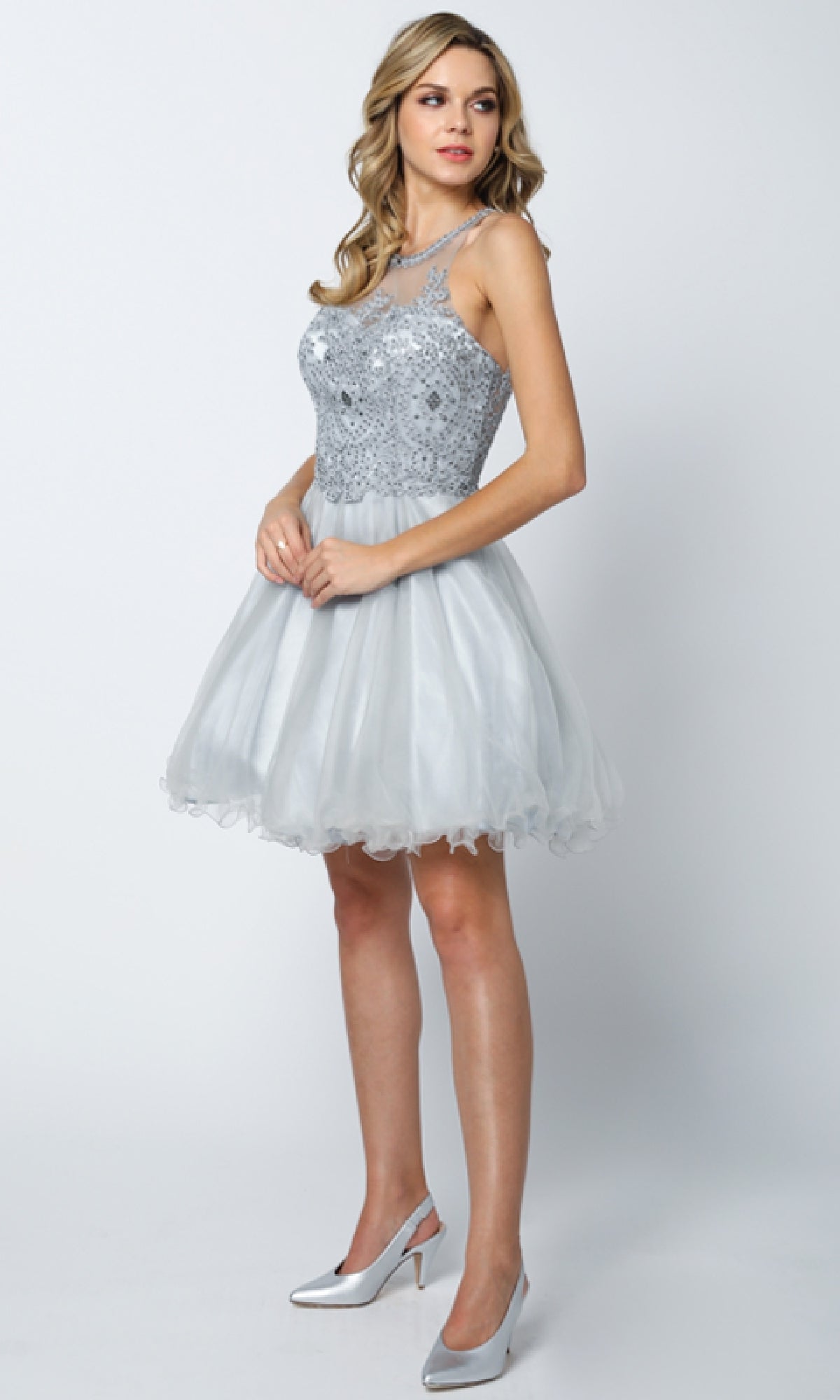 A woman in the Juliet 826 short hoco dress, featuring a sleeveless light gray lace bodice and an A-line tulle skirt, with silver heels, stands against a plain light background.