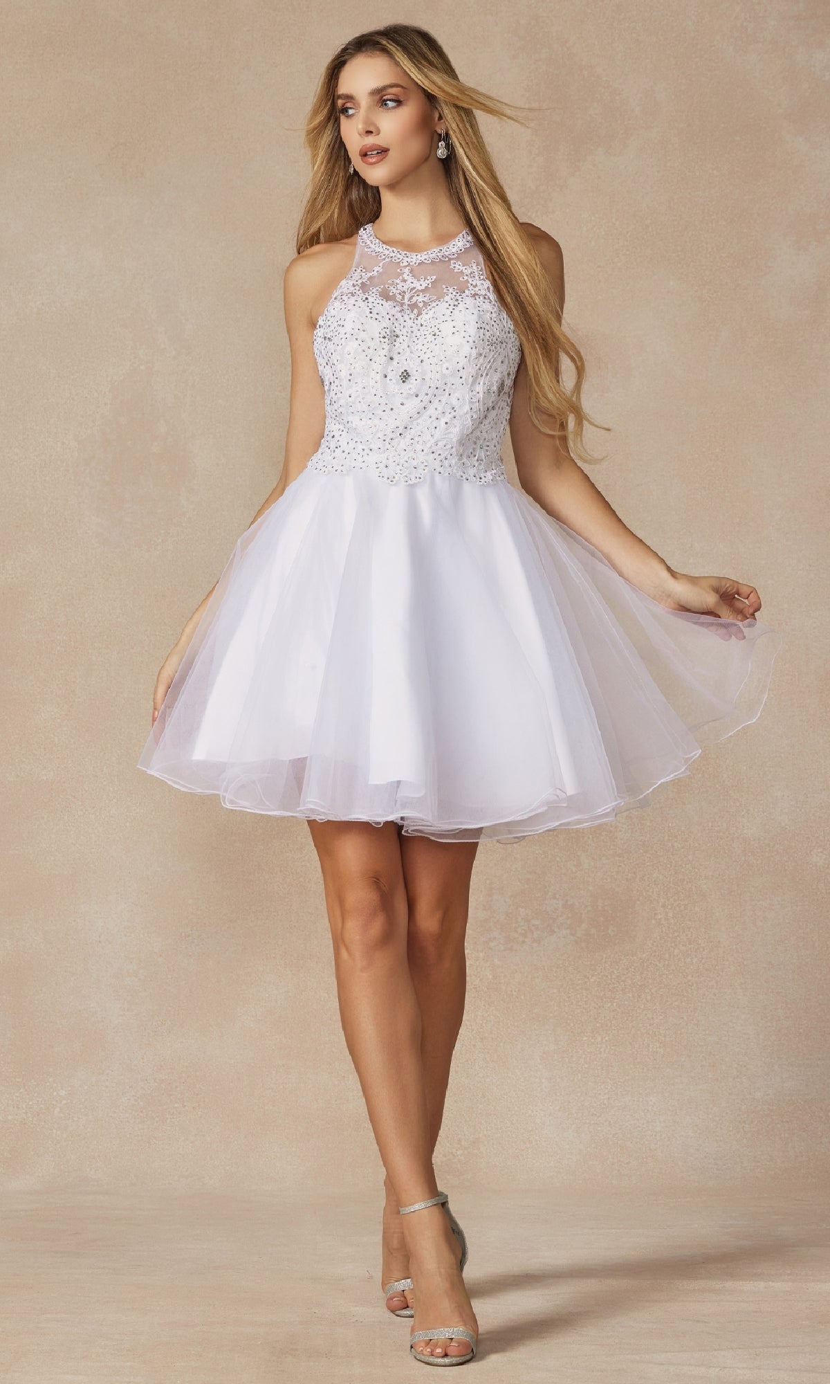 Woman in the Juliet 826 short hoco dress featuring a white sleeveless design, sheer embellished bodice, A-line tulle skirt, and paired with silver high-heeled sandals.