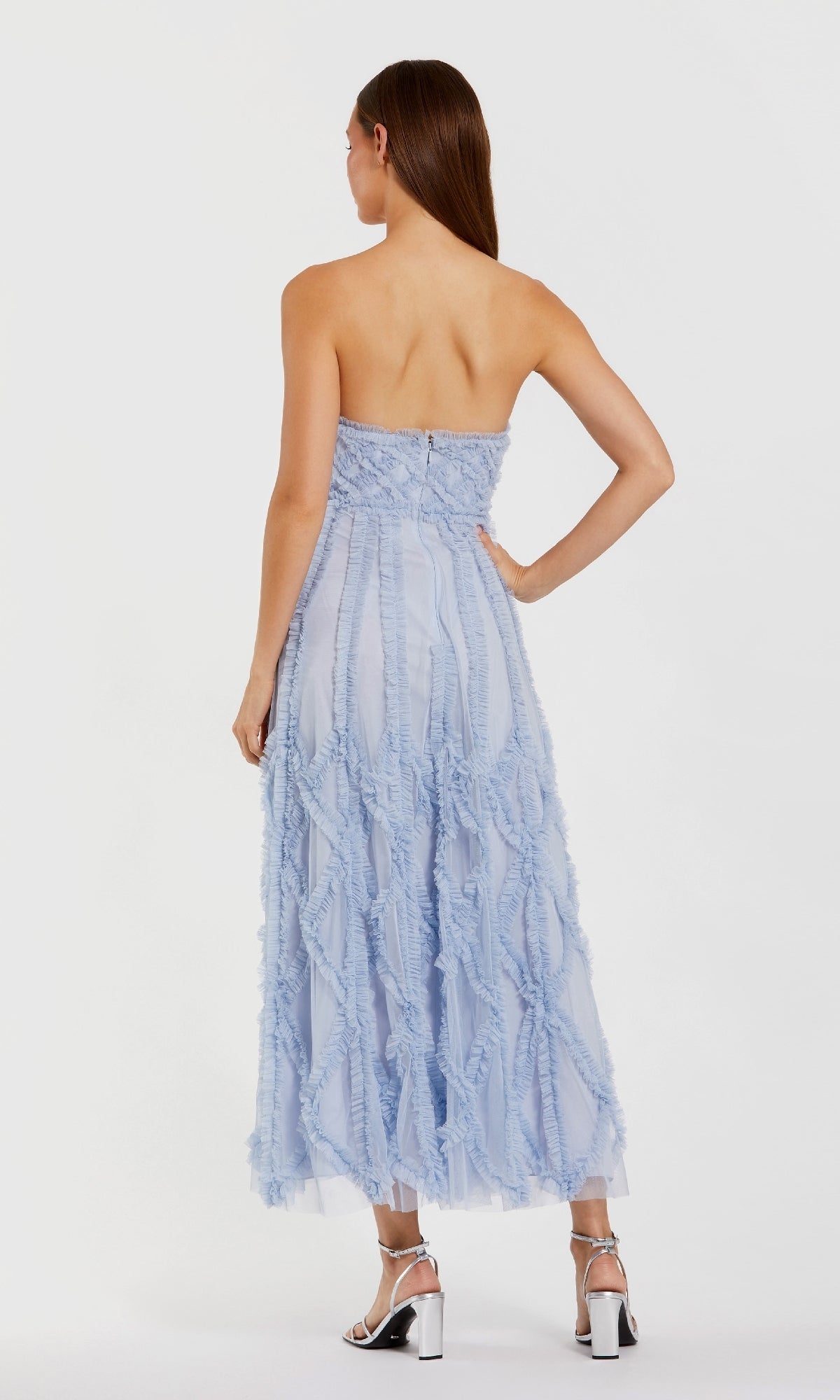 A woman faces away, wearing the Mac Duggal 8277 Periwinkle Wedding Guest Dress—strapless with a textured ankle-length skirt—and metallic heeled sandals, set against a plain white background.