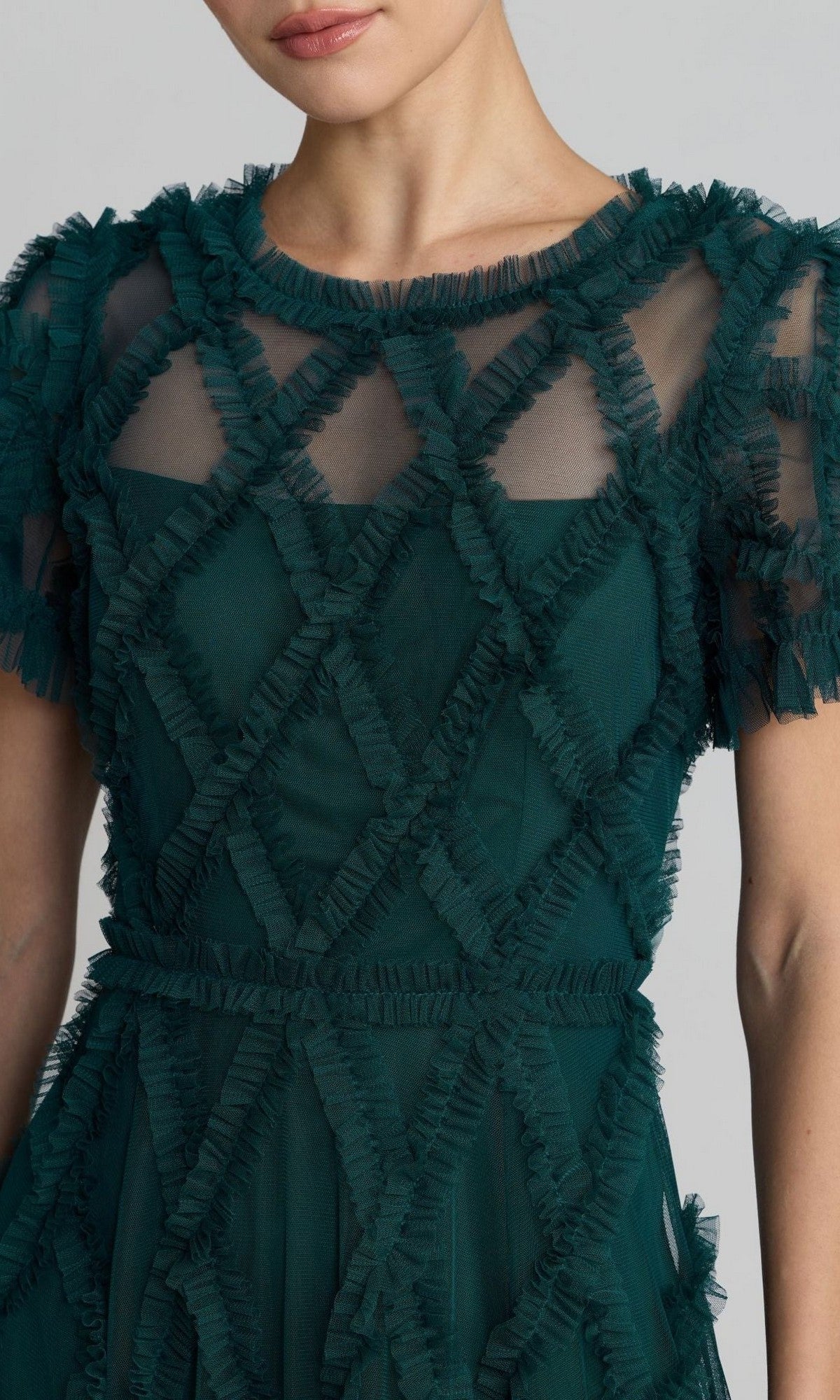 A woman wears the Mac Duggal 8278 short sleeve midi formal dress in dark green, featuring geometric ruffle details and sheer panels at the neckline and sleeves.