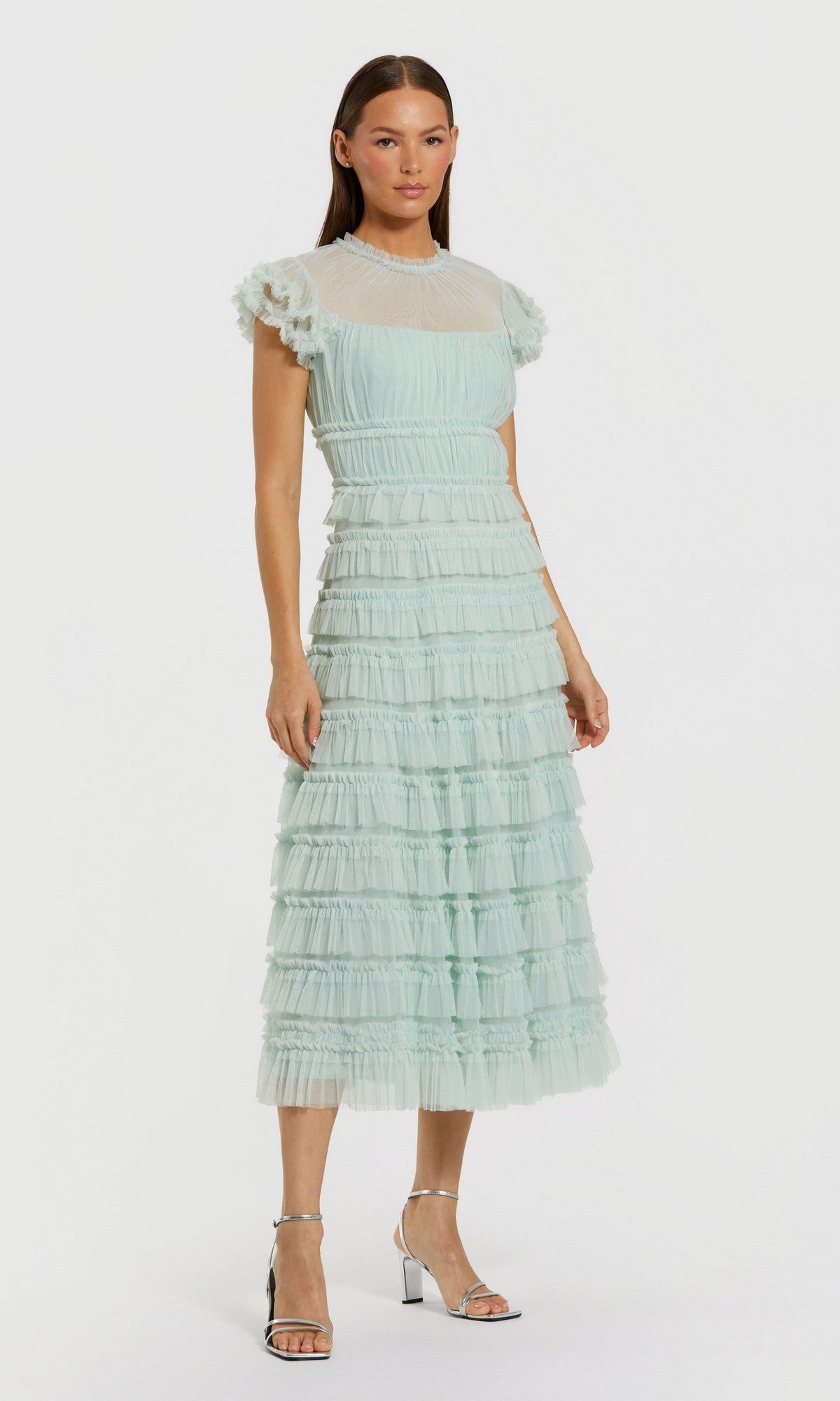 A woman wears the mint Midi Wedding Guest Dress: Mac Duggal 8285 with a sheer high neck, fit-and-flare silhouette, and silver heels, standing against a plain white background.
