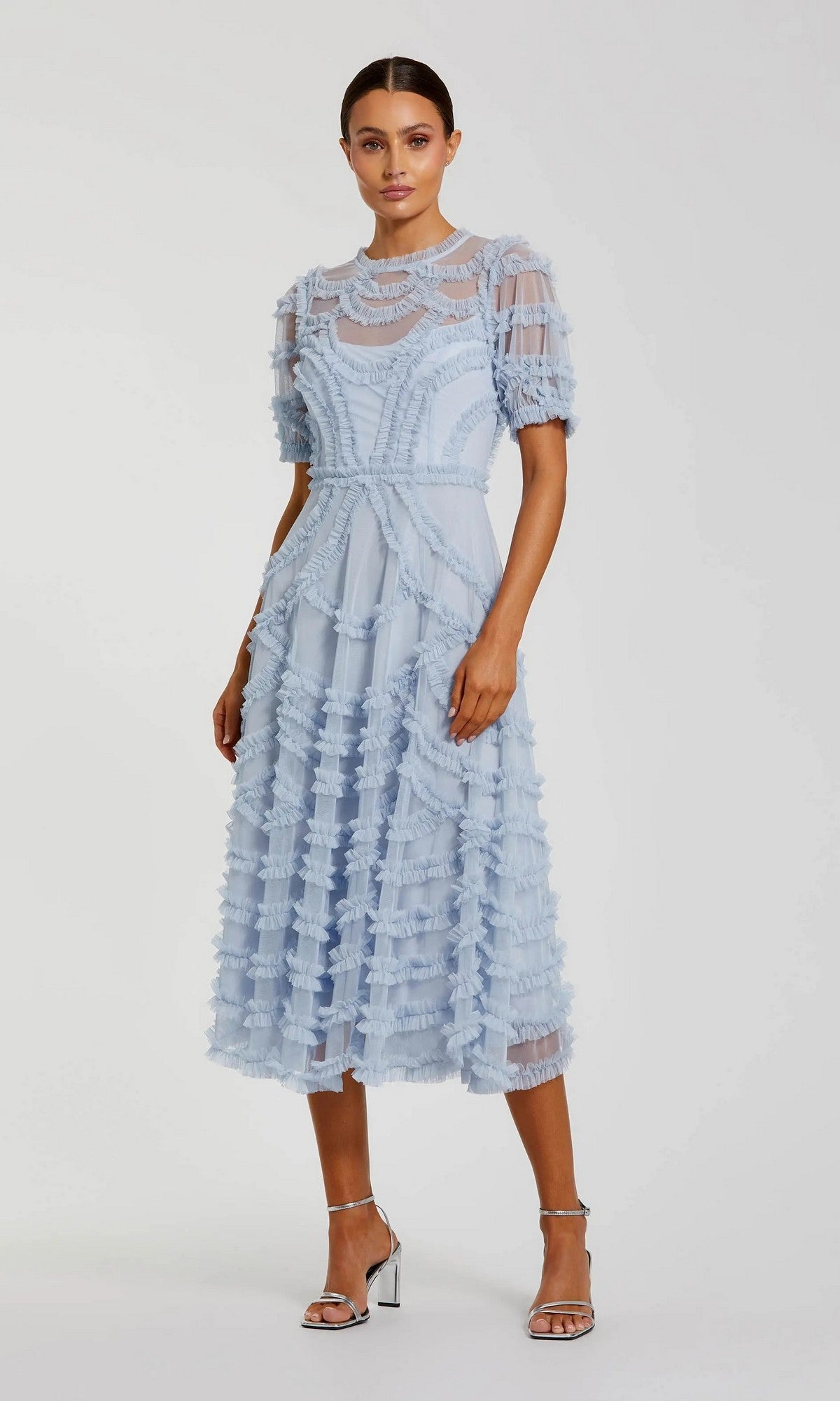 A woman models the Midi Party Dress: Mac Duggal 8288 in periwinkle, an elegant A-line midi dress with micro-ruffle detailing and sheer short sleeves, styled with silver heeled sandals against a plain white background.