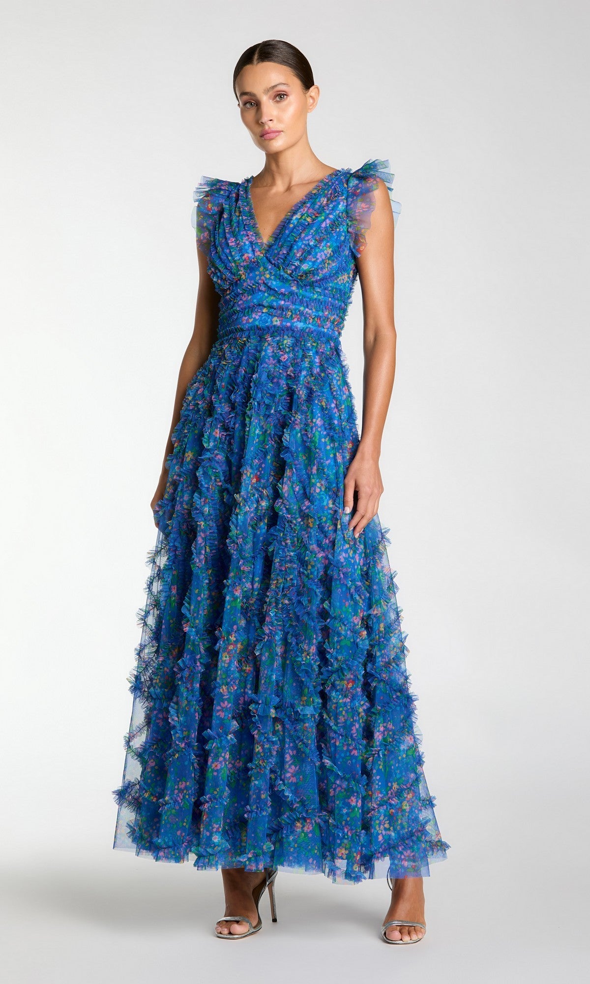 A woman in a Mac Duggal 8303 long formal dress, sleeveless with a blue multi floral pattern and floor-length ruffled tulle skirt, stands against a plain background.