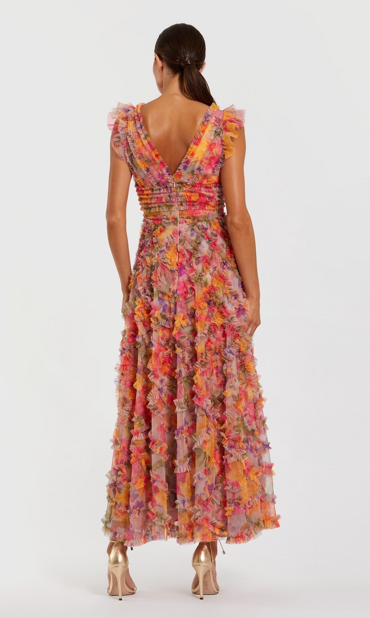 A woman stands with her back to the camera, wearing the vibrant Mac Duggal 8303 long formal dress featuring a V-back, paired with gold high heels.