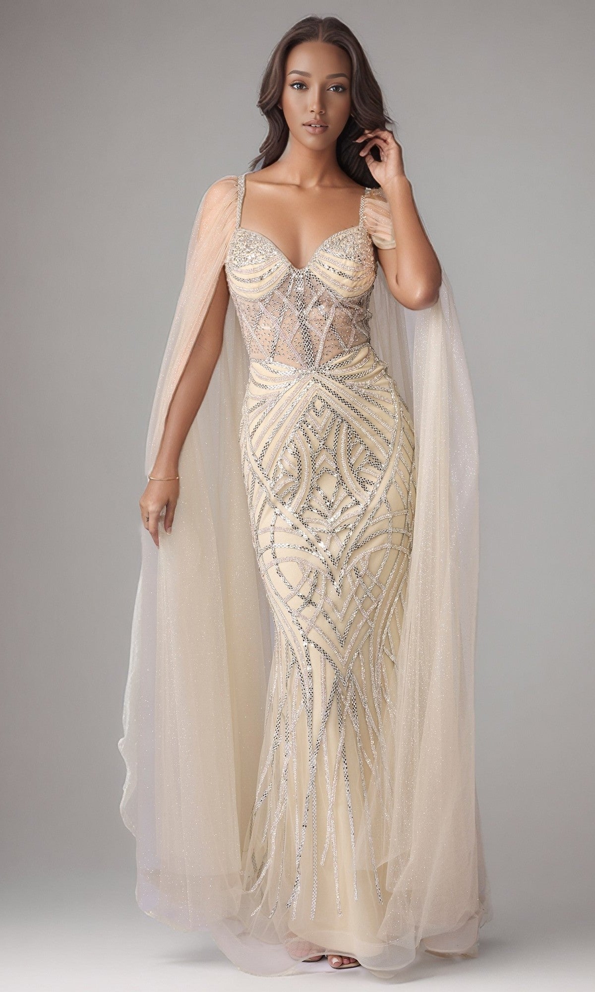 A woman in the Nina Canacci 8305 long formal dress, champagne/silver color, adorned with sparkling beadwork and sheer cape sleeves, stands against a neutral background.