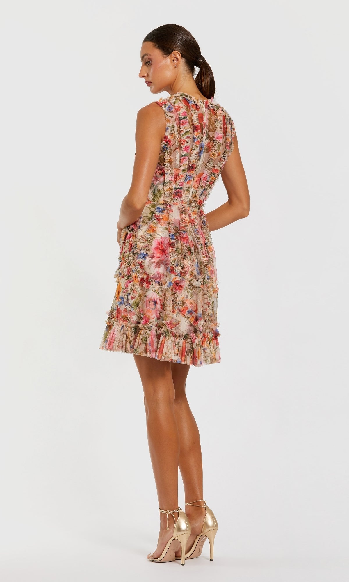 A woman faces away, wearing the Mac Duggal 8307 high-neck print wedding-guest dress with ruffle details and nude heels, set against a plain white background.