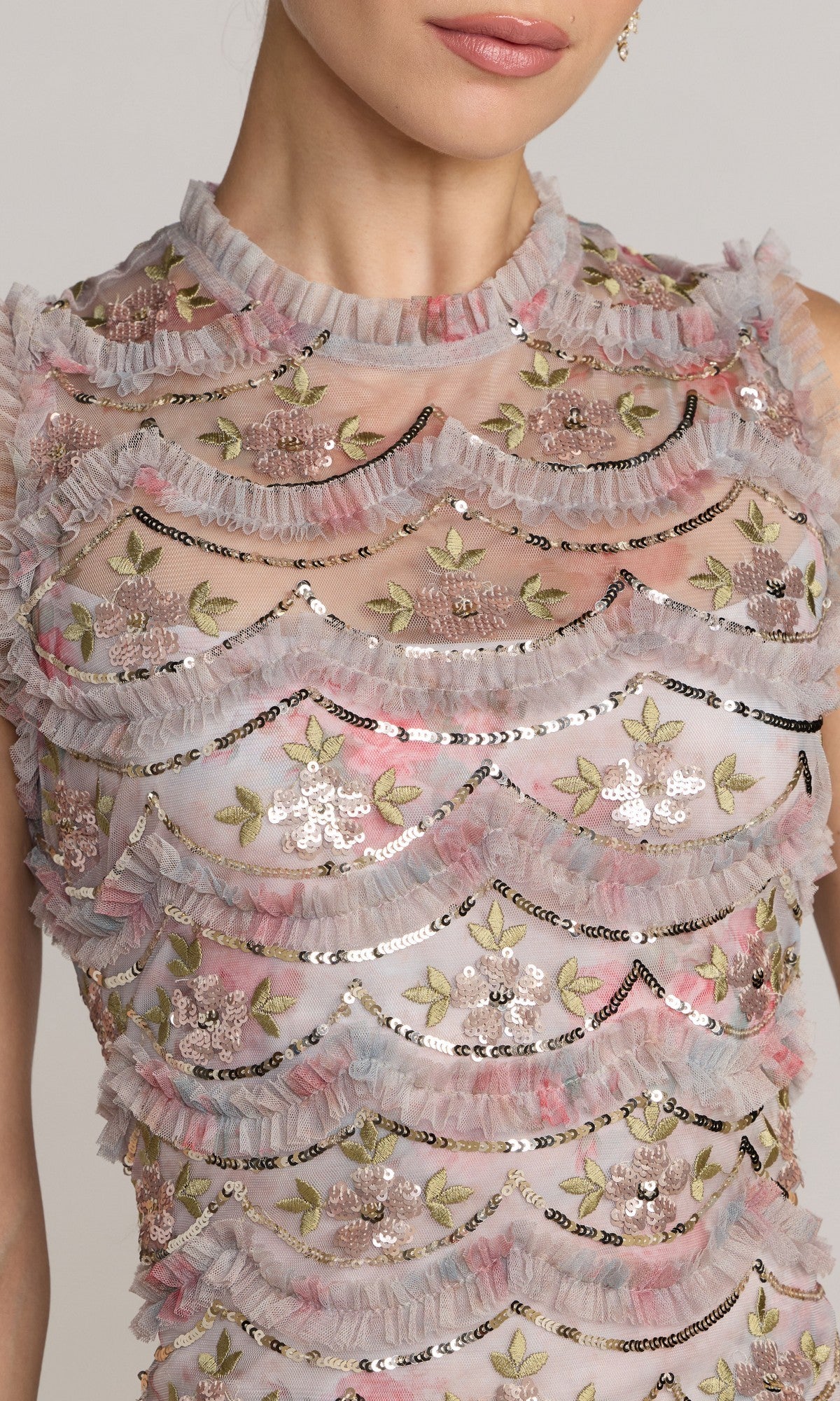 Close-up of a person wearing the Midi Party Dress: Mac Duggal 8412โa sheer, sleeveless design featuring floral embroidery, sequins, and layered ruffled trim in pink, gold, and silver tones.