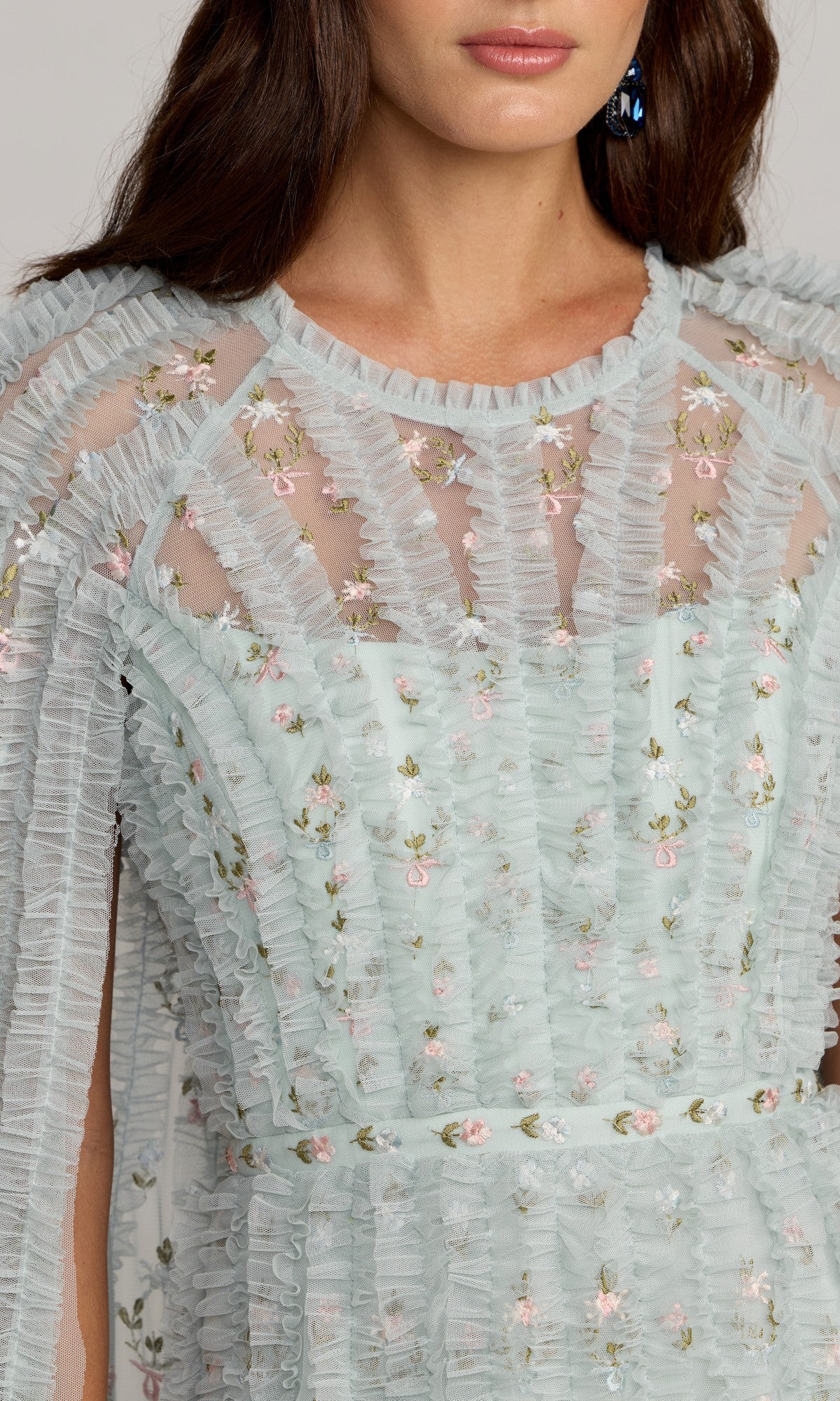 A woman wears the Mac Duggal 8444 long formal dress, featuring light blue sheer ruffled fabric with vertical pleats and floral embroidery; only her upper torso and part of her face are visible.