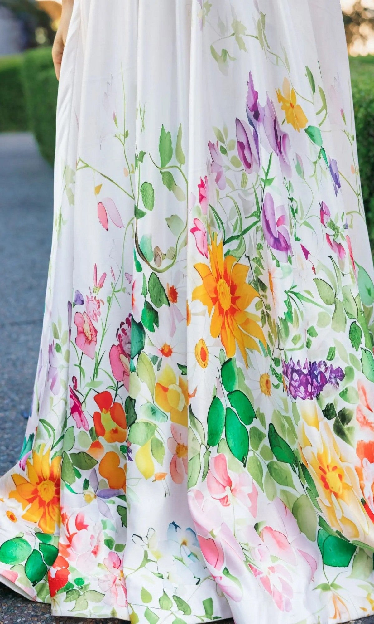 A close-up of the Mac Duggal 8470 long formal dress in white satin, featuring a floor-length silhouette adorned with a vibrant floral print in yellow, purple, pink, and green.