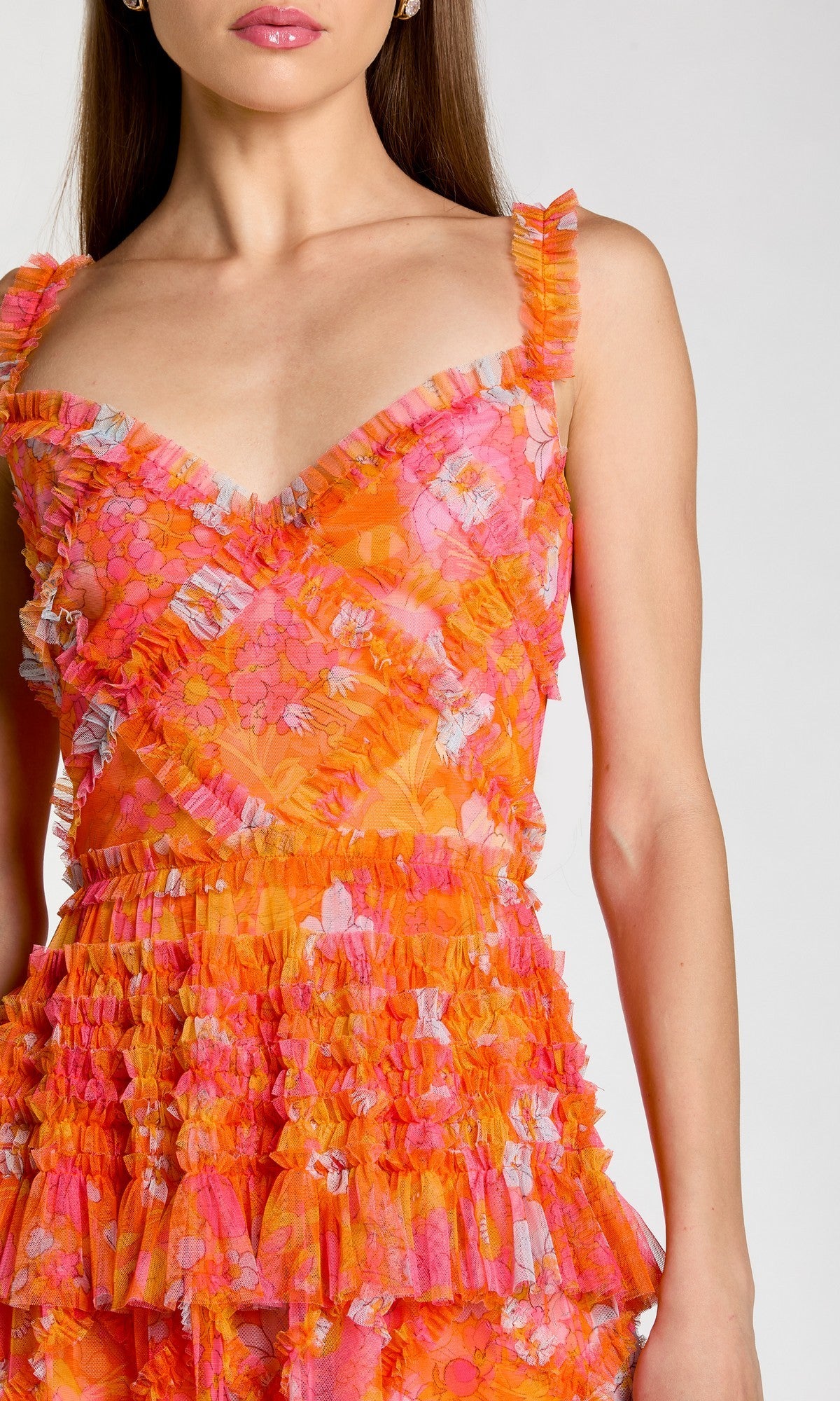 A woman wears the Mac Duggal 8475 Long Formal Dress, a sleeveless orange and pink design with floral patterns, ruffled straps, and a ruffled fit-and-flare skirt; photographed from shoulders to above the knees against a plain background.